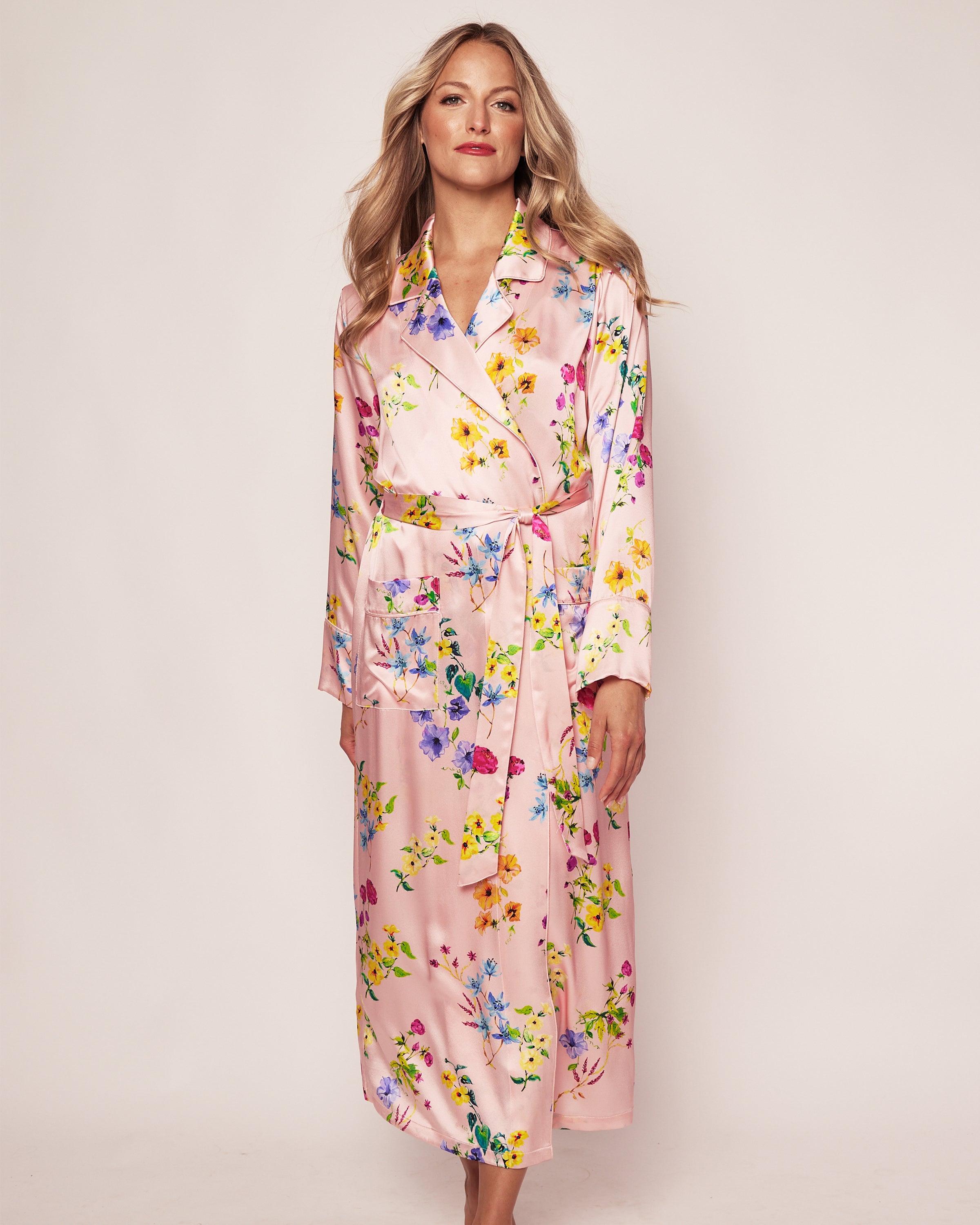 A person stands against a plain background, looking forward while wearing the Womens Silk Robe in Blush Brilliant Botanical by Petite Plume.