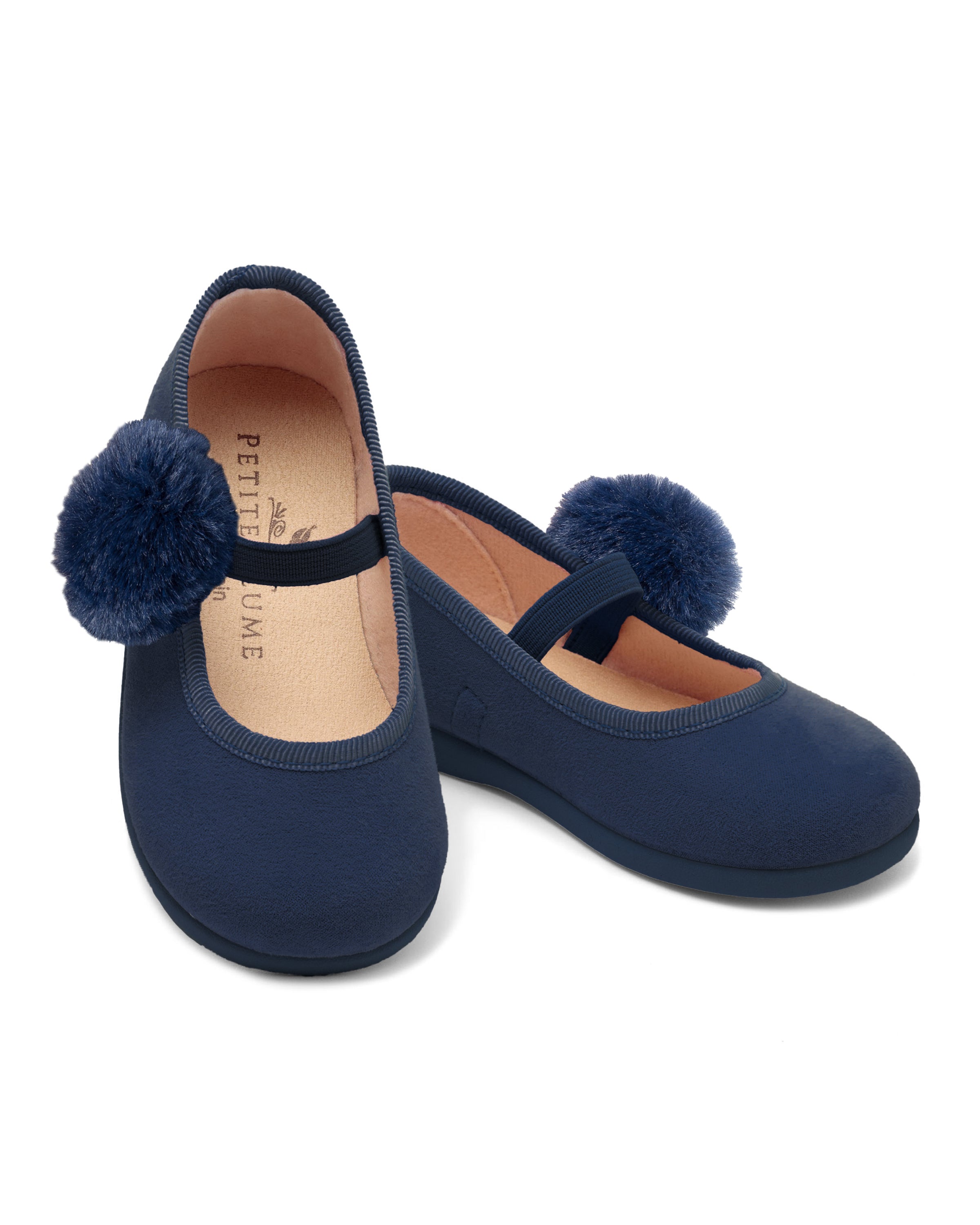 The Kids Delphine Slipper by Petite Plume is made of navy suede, featuring large pom-poms on the toes and a simple strap. The beige insoles are stamped with the logo, and they are elegantly displayed against a white background.