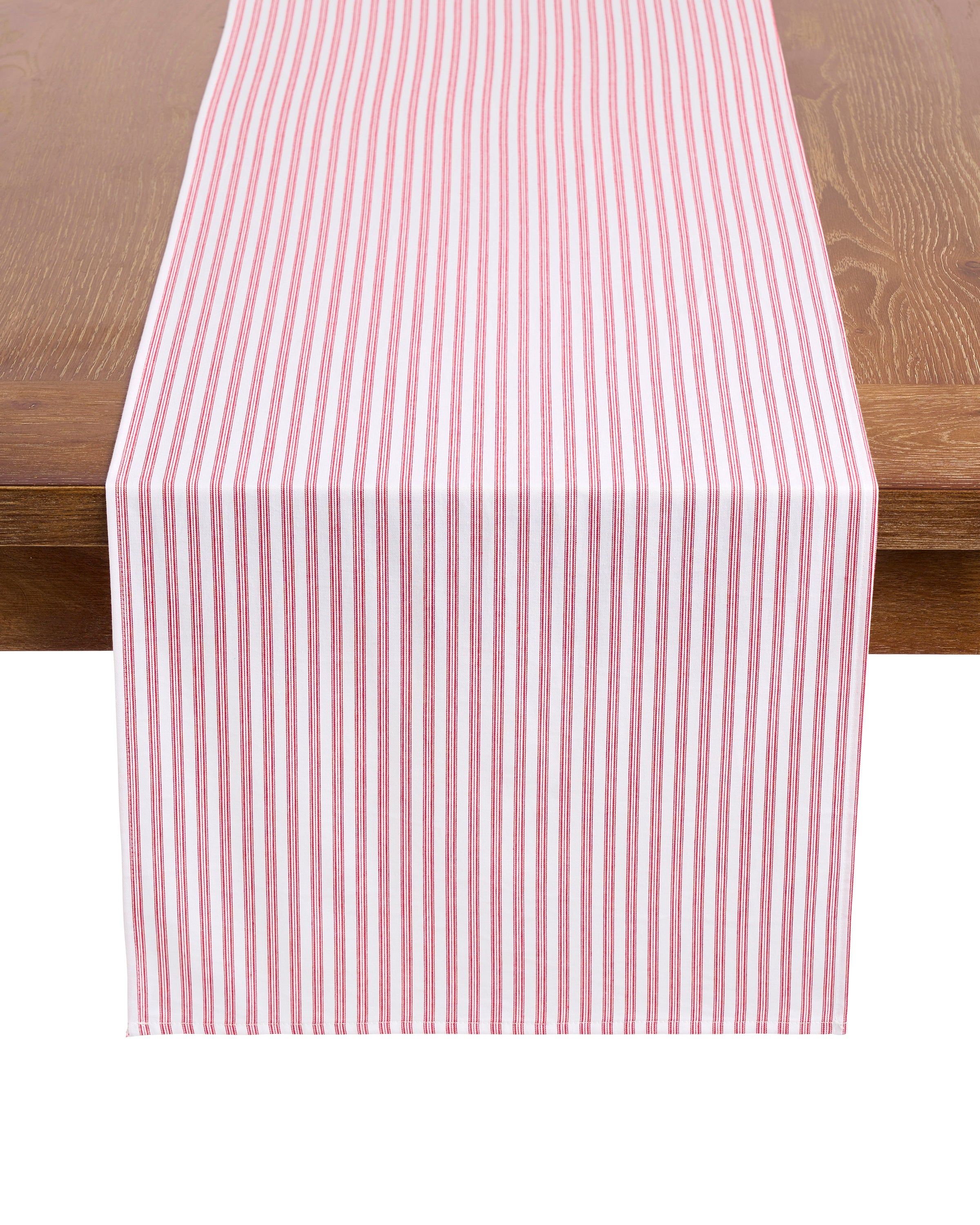 Elevate your festive tablescape with the Signature Twill Table Runner in Antique Red Ticking by Petite Plume, featuring red and white vertical stripes that complement your favorite table linens on a wooden surface.