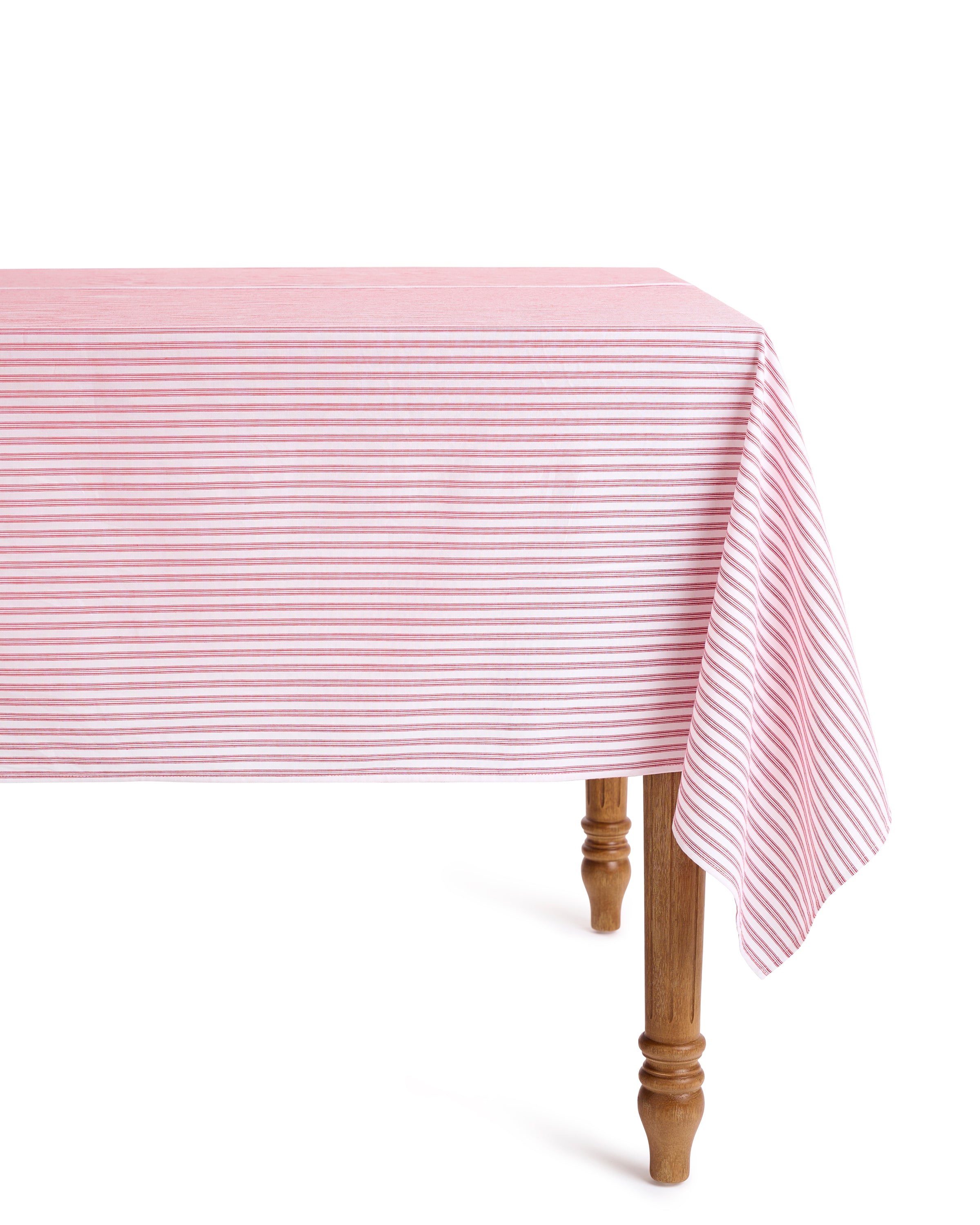 A wooden table with a Signature Twill Tablecloth in Antique Red Ticking by Petite Plume partially draped over it. The cloth showcases its crisp linear pattern and is enhanced by carved legs, offering an elegant touch for a festive tablescape that highlights its simple yet sophisticated design.