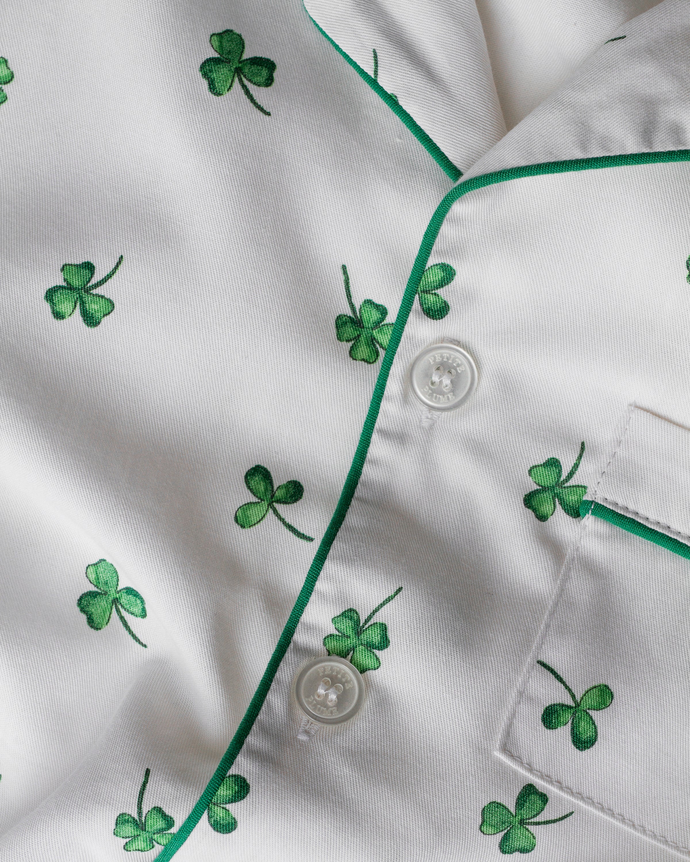 The Kids Twill Pajama Set in Shamrocks by Petite Plume features a white shirt with green piping and tiny four-leaf clovers, accompanied by three buttons and a right-side pocket, offering charm and comfort within the Shamrocks Collection for luxurious sleepwear.