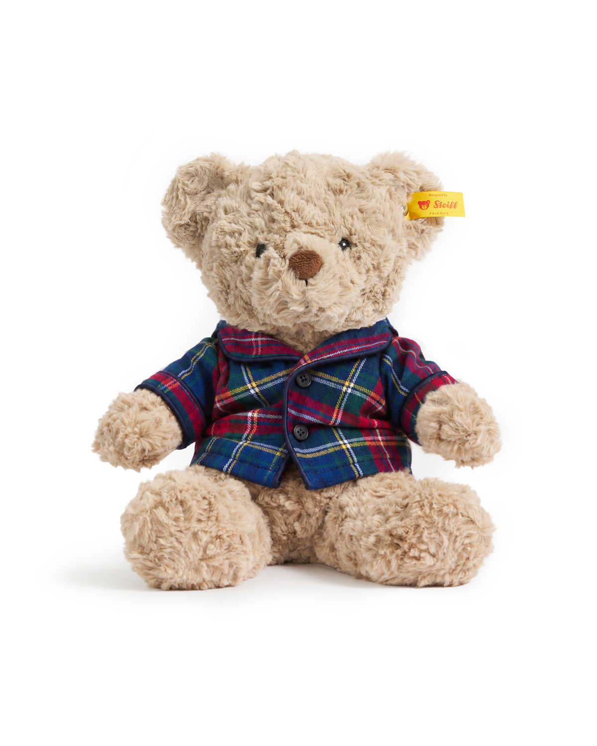 A tan plush Petite Plume x Steiff Teddy Bear in Windsor Tartan wearing a red, green, and blue plaid button-down pajama top.