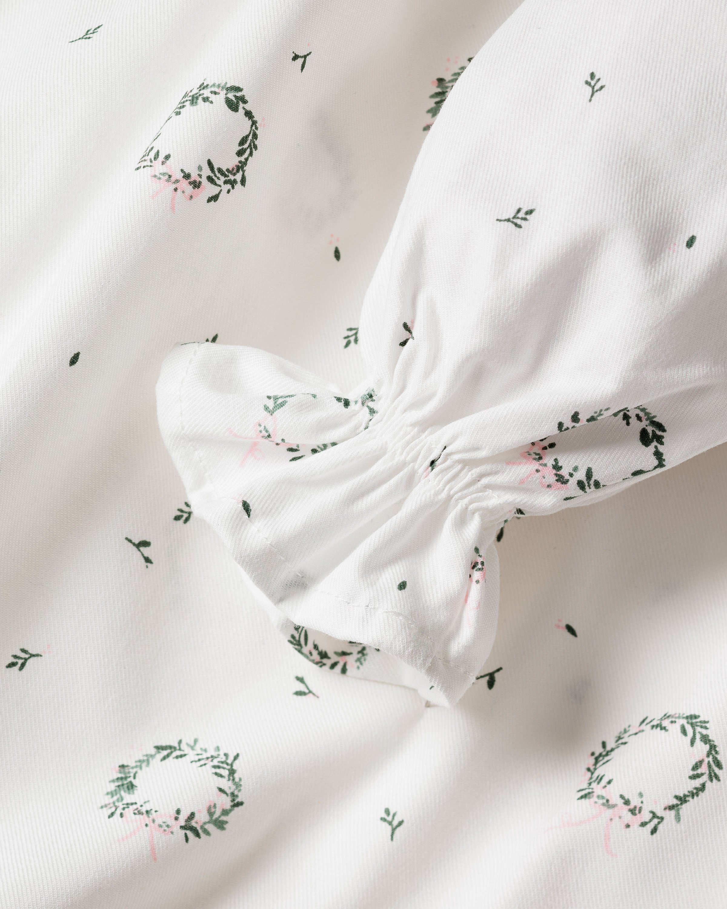 Close-up of Petite Plumes Girls Twill Delphine Nightgown in Somerset Wreath, featuring soft, lightweight white fabric with green and pink wreath and floral patterns. The chemical-free flame-retardant material is gathered at one end, resembling a puff sleeve or scrunchie—ideal for childrens sleepwear.