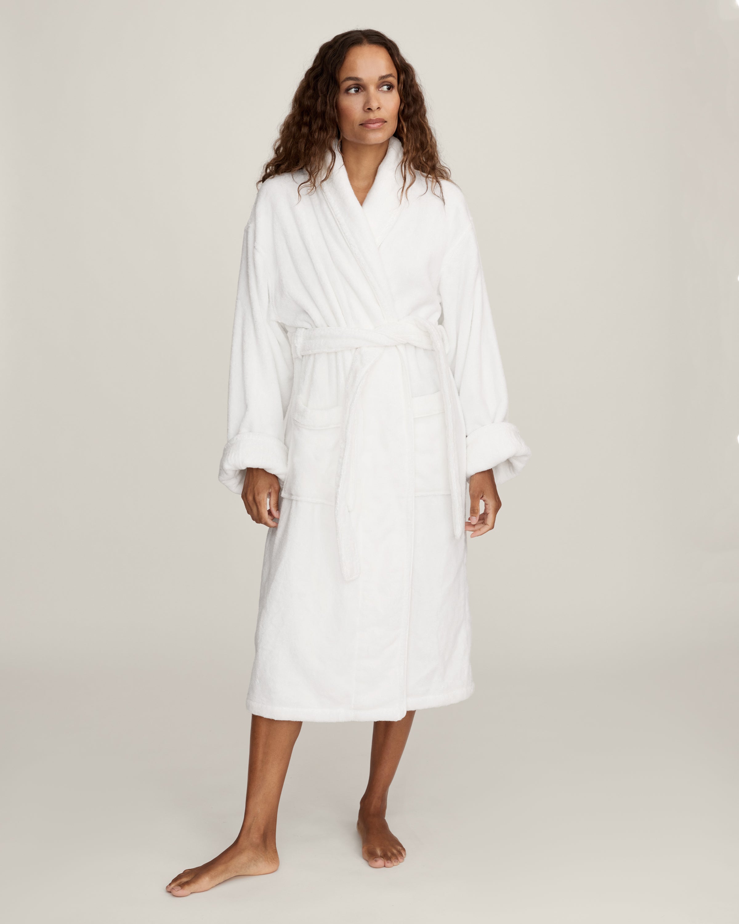 The Unisex Luxe Terry Robe in White features long sleeves, a shawl collar, two front pockets, and a waist tie belt, displayed against a white background.