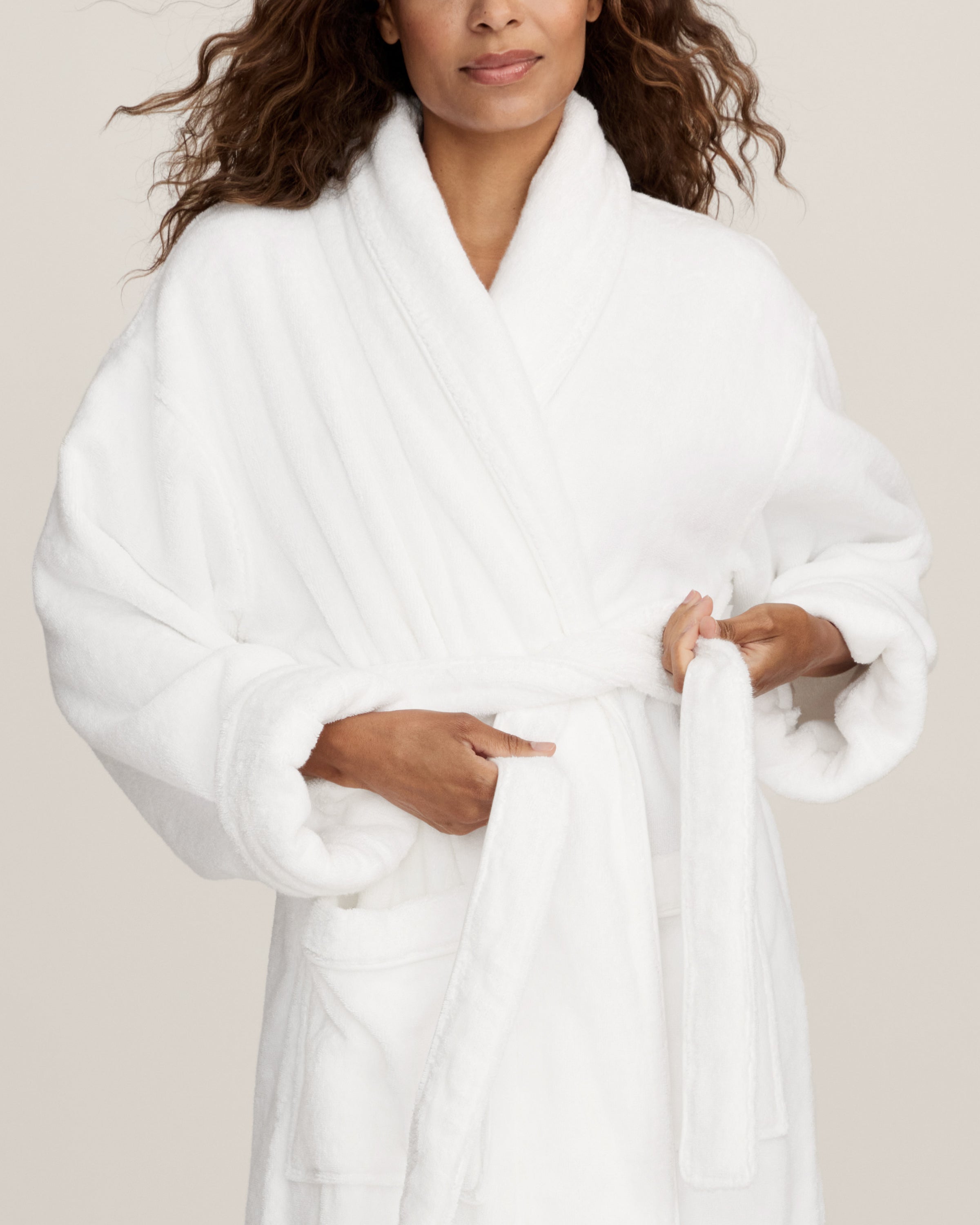 The Unisex Luxe Terry Robe in White features long sleeves, a shawl collar, two front pockets, and a waist tie belt, displayed against a white background.