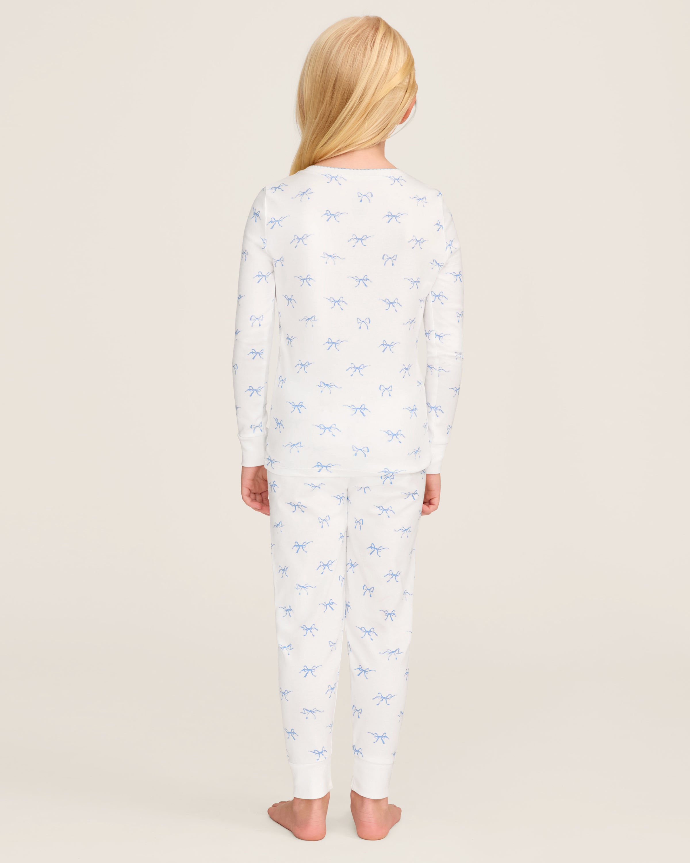 The Kid's Pima Snug Fit Pajama Set in Something Blue Bows features a long-sleeve white top and matching pants with a light blue bow pattern, crew neckline, and soft, comfortable fabric.