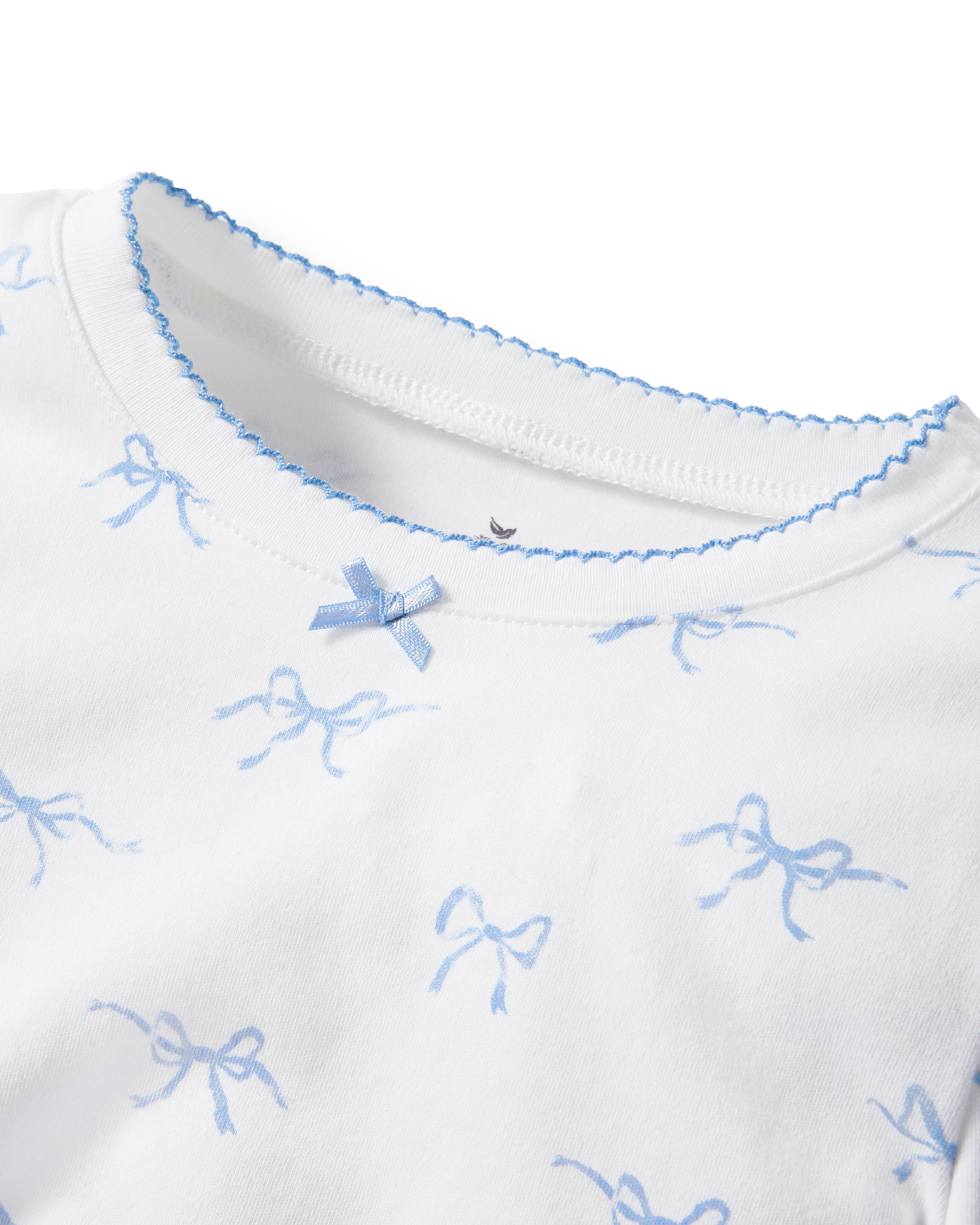 The Kid's Pima Snug Fit Pajama Set in Something Blue Bows features a long-sleeve white top and matching pants with a light blue bow pattern, crew neckline, and soft, comfortable fabric.