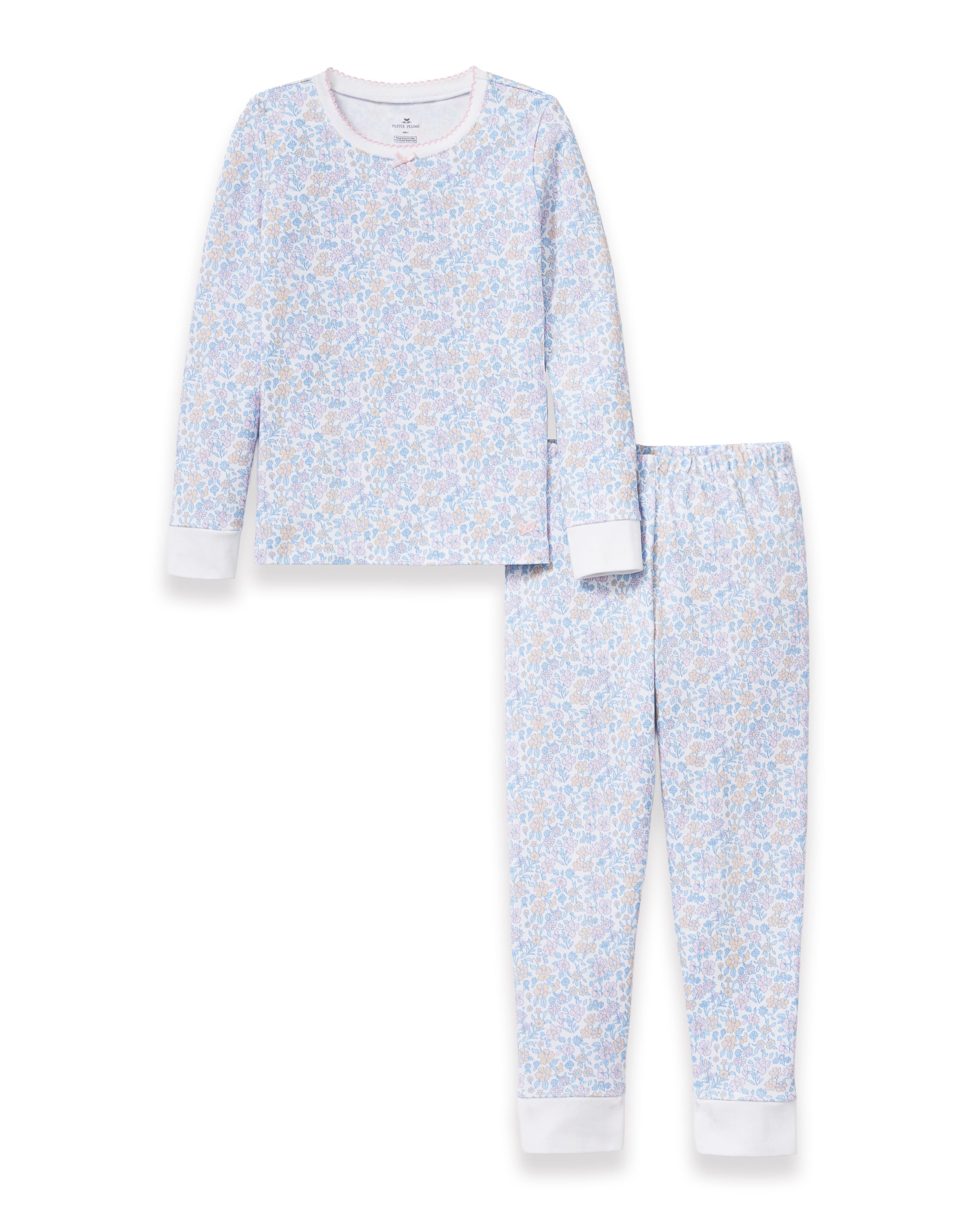 A young girl with long, wavy hair stands barefoot on a plain background, wearing the Kid's Pima Snug Fit Pajama Set in Fleur Blanche. She looks slightly to the side with a relaxed expression.