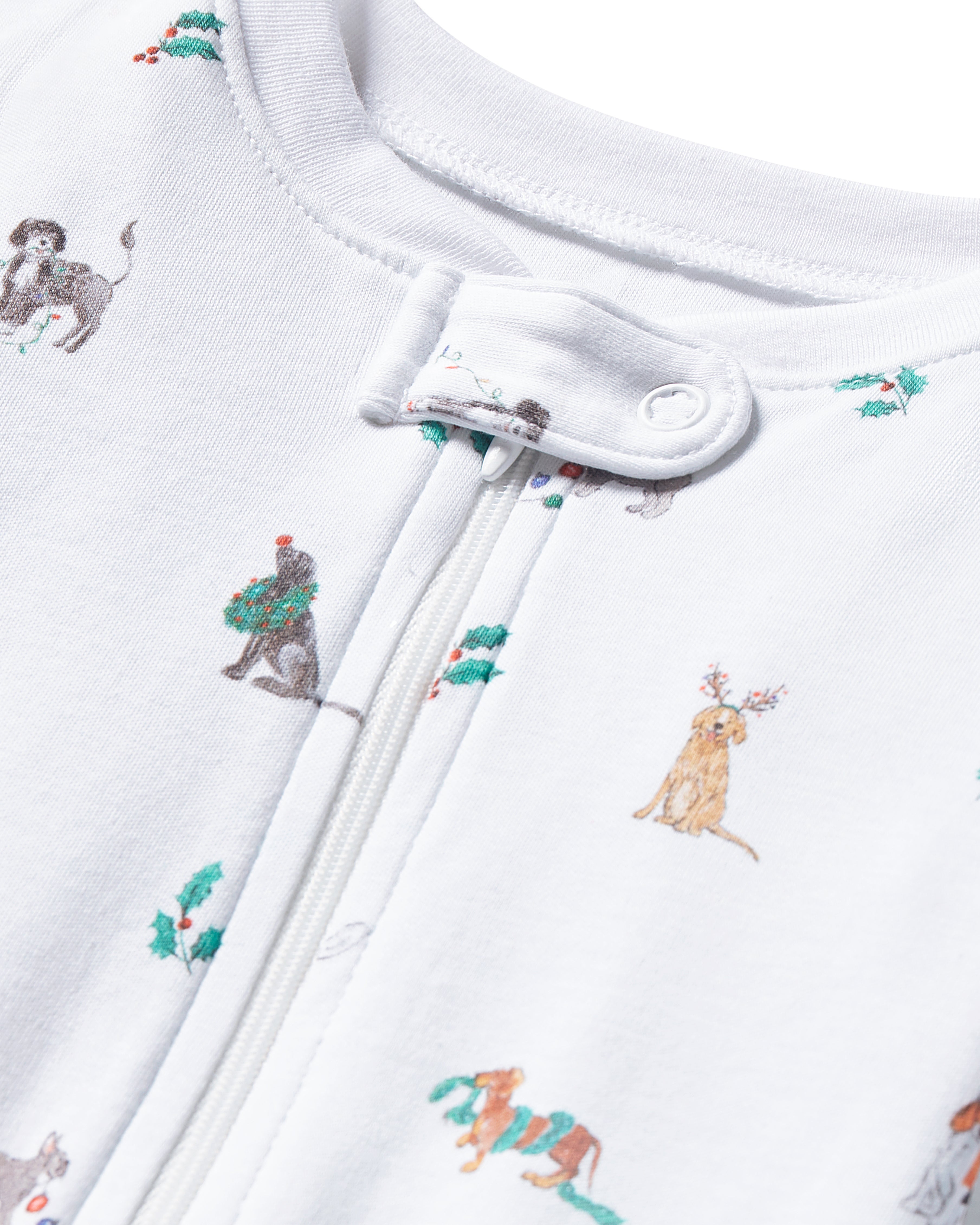 Close-up of Petite Plumes Babys Pima Romper in Jingle Paws, featuring soft white fabric with holiday dog illustrations. Some dogs wear wreaths and antlers. A central zipper with a snap button ensures secure closure, making it ideal sleepwear.