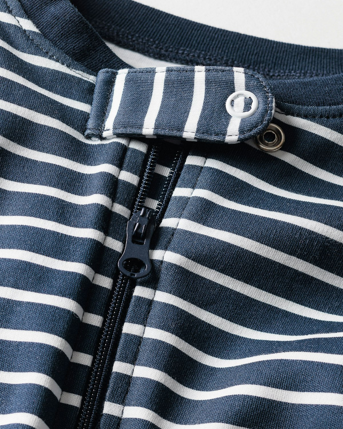 Close-up of Petite Plumes Babys Pima Romper in Navy Stripe with a zipper. Made from soft Pima cotton, it includes a buttoned flap at the neckline and features navy blue and white horizontal stripes.