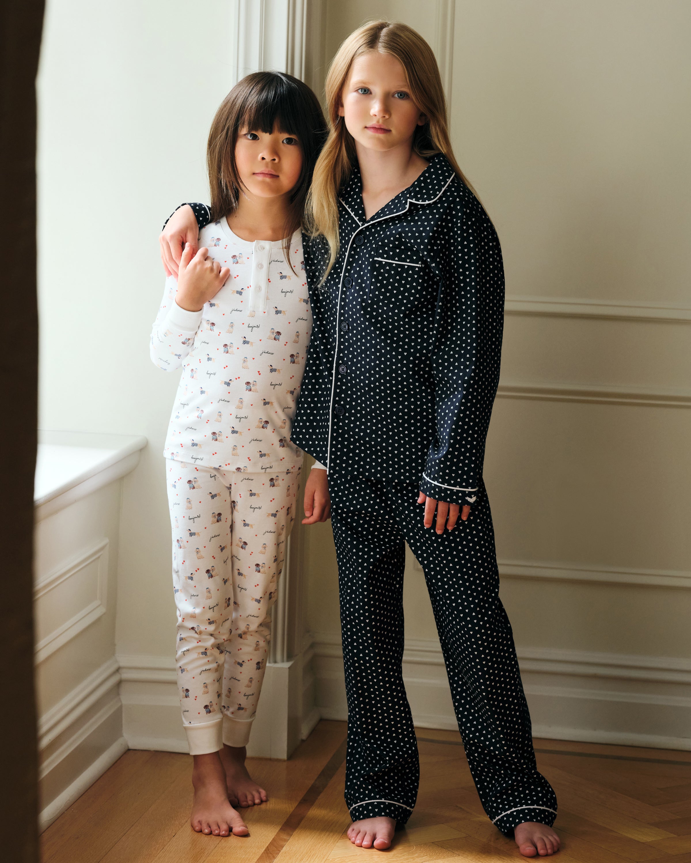 The Kid's Pima Snug Fit Pajama Set in Le Woof is a white long-sleeve pajama set with matching pants, featuring a colorful all-over cartoon dog and bone print, plus cuffed sleeves and ankles for a snug fit.