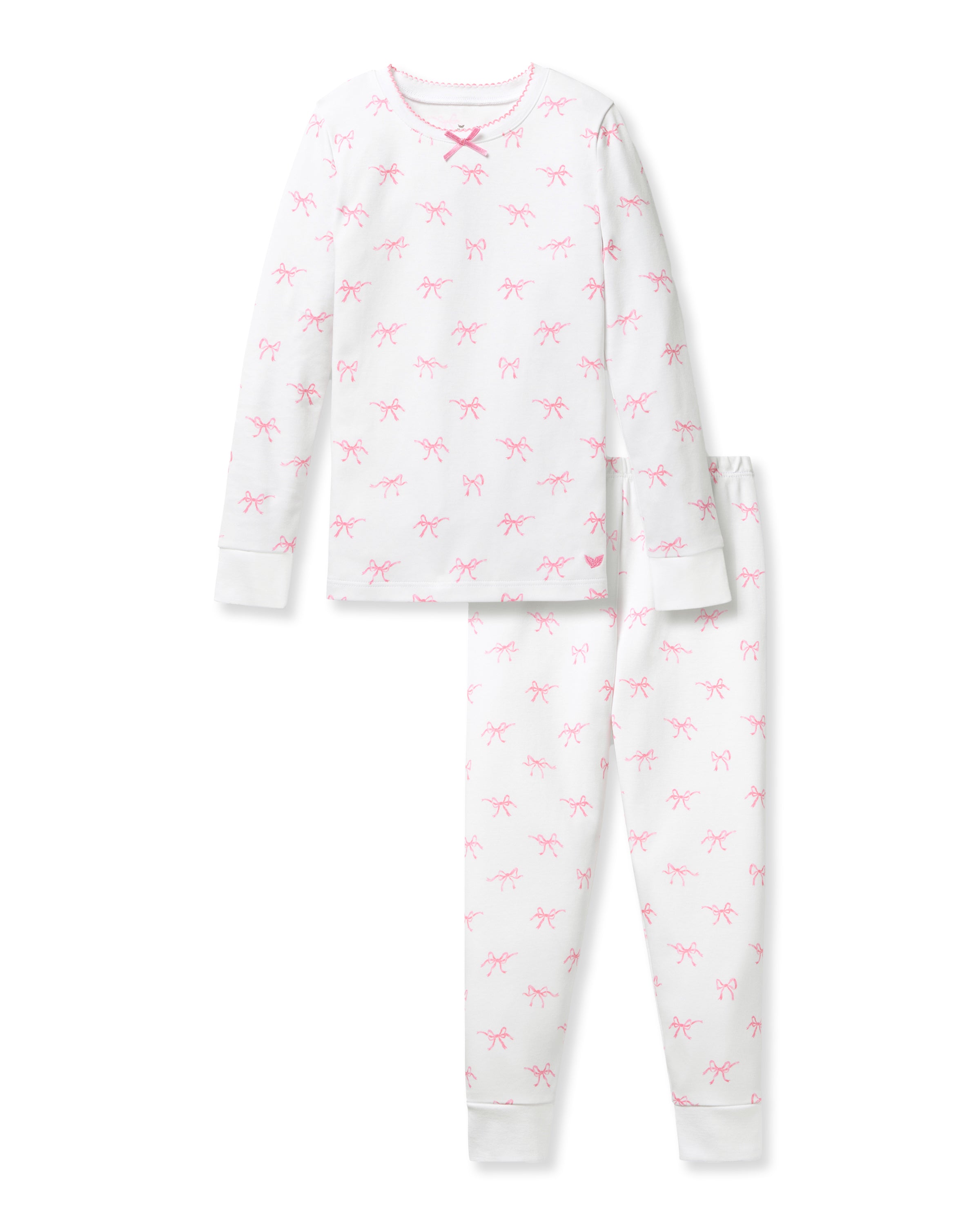 A confident young girl with long brown hair wears the Petite Plume Kids Pima Snug Fit Pajama Set in Blushing Bows, featuring a long sleeve top and pants made from soft Pima cotton with small pink patterns against a plain light-colored background.