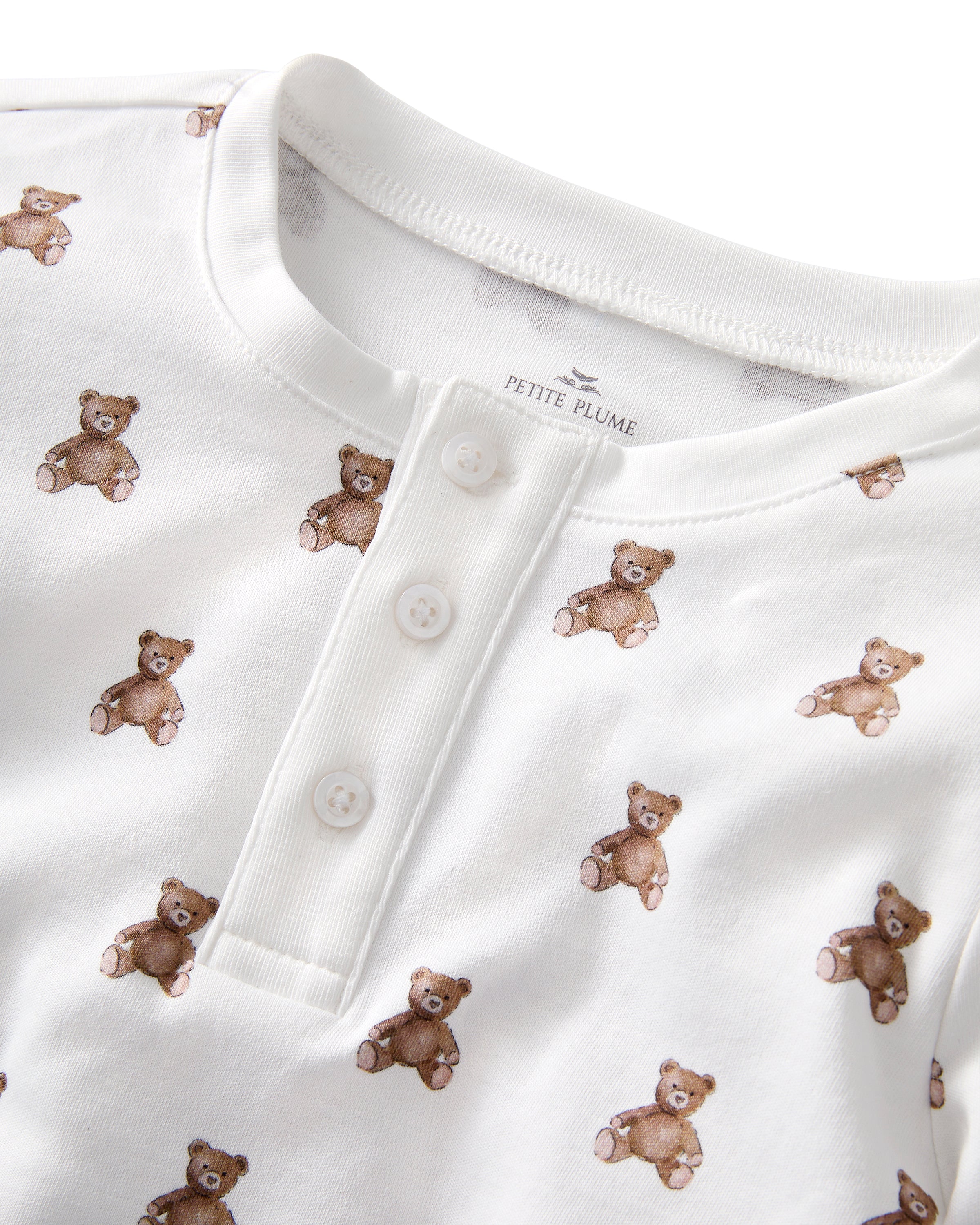The Kid's Pima Snug Fit Pajama Set in Teddy Tales features a white long-sleeve buttoned top and elastic waist pants with ribbed cuffs, both printed all over with brown teddy bears. Suitable for children.