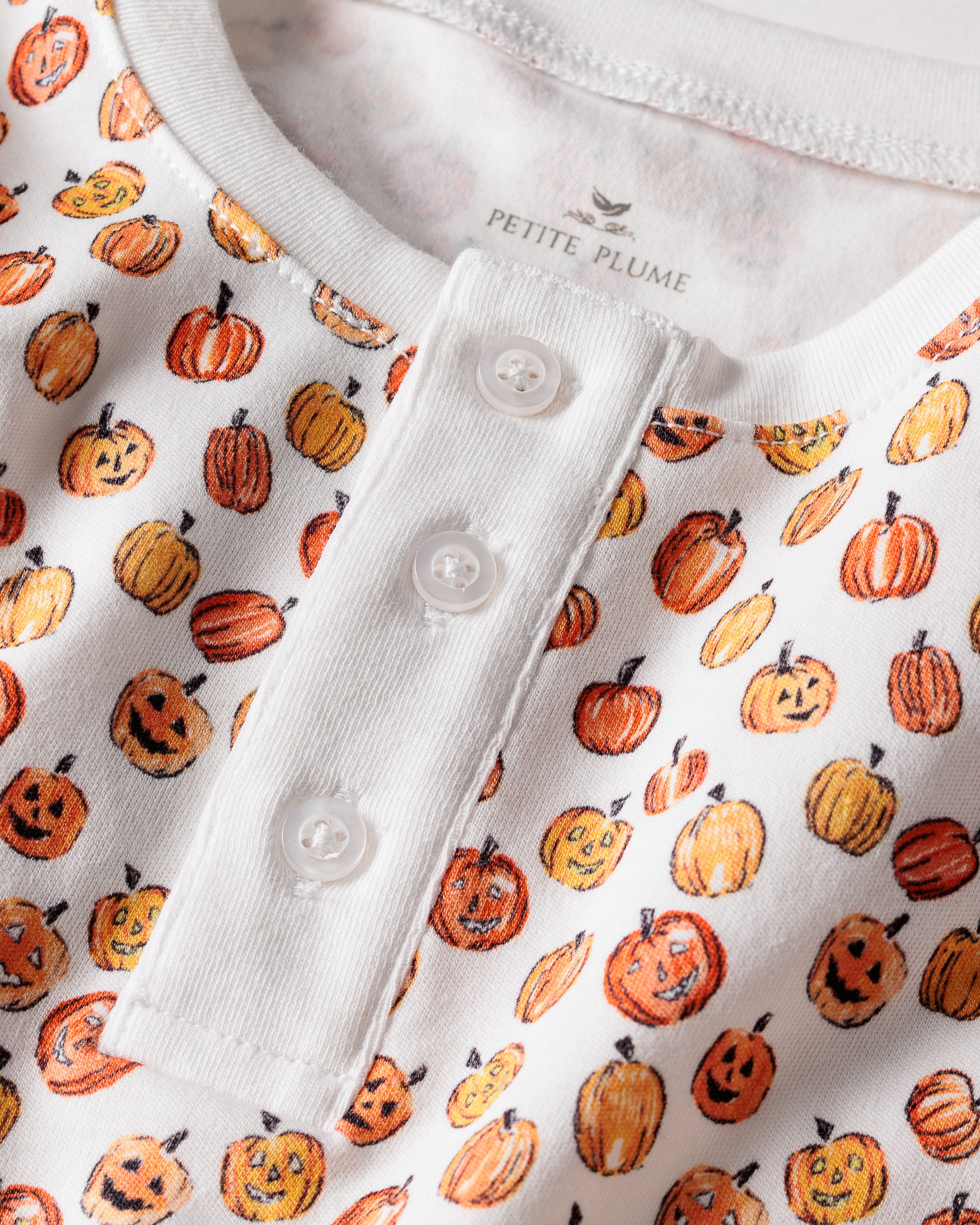 Close-up of Petite Plumes Kids Pima Snug Fit Pajama Set in Pumpkin Patch, showcasing soft Pima Cotton with vibrant orange and yellow smiling pumpkins. The Halloween pajamas feature a buttoned placket with three white buttons.