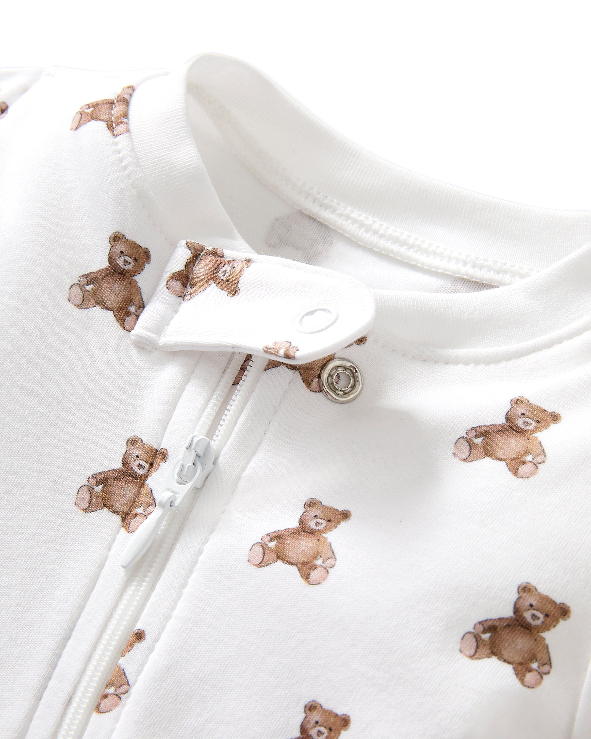 The Baby's Pima Romper in Teddy Tales features a white base with an all-over brown teddy bear print, long sleeves, a zip closure from neck to leg, and a snap button at the collar.
