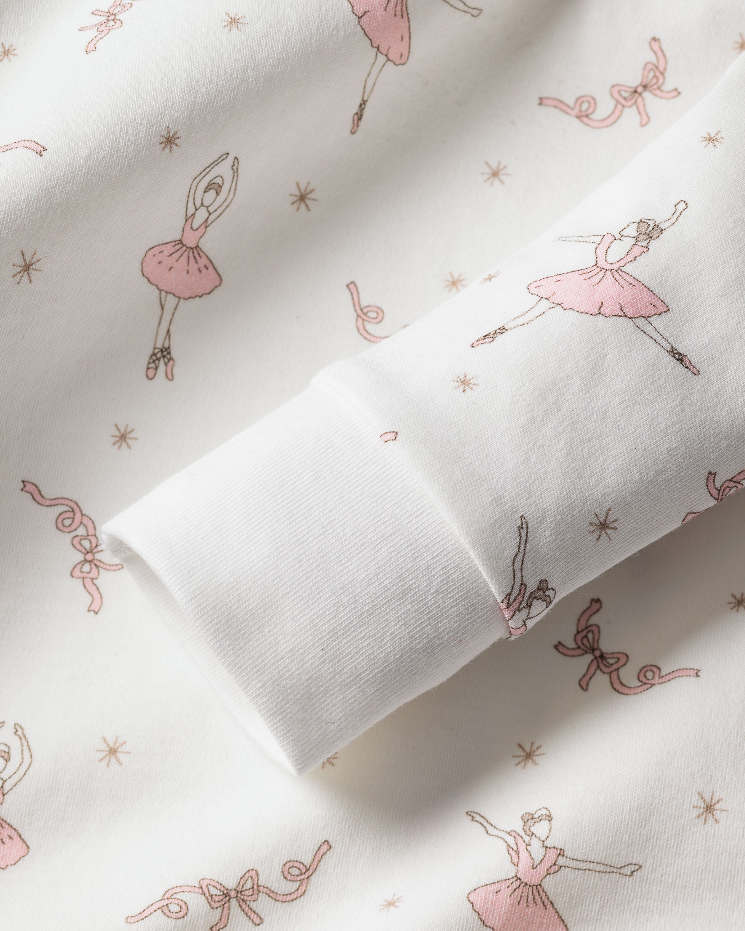 The Kids Pima Snug Fit Pajama Set in Sugar Plum Fairy by Petite Plume showcases soft Pima cotton adorned with charming pink ballerinas, small stars, and ribbons. The long sleeve top includes rolled-up sleeves to accentuate the delicate pattern.