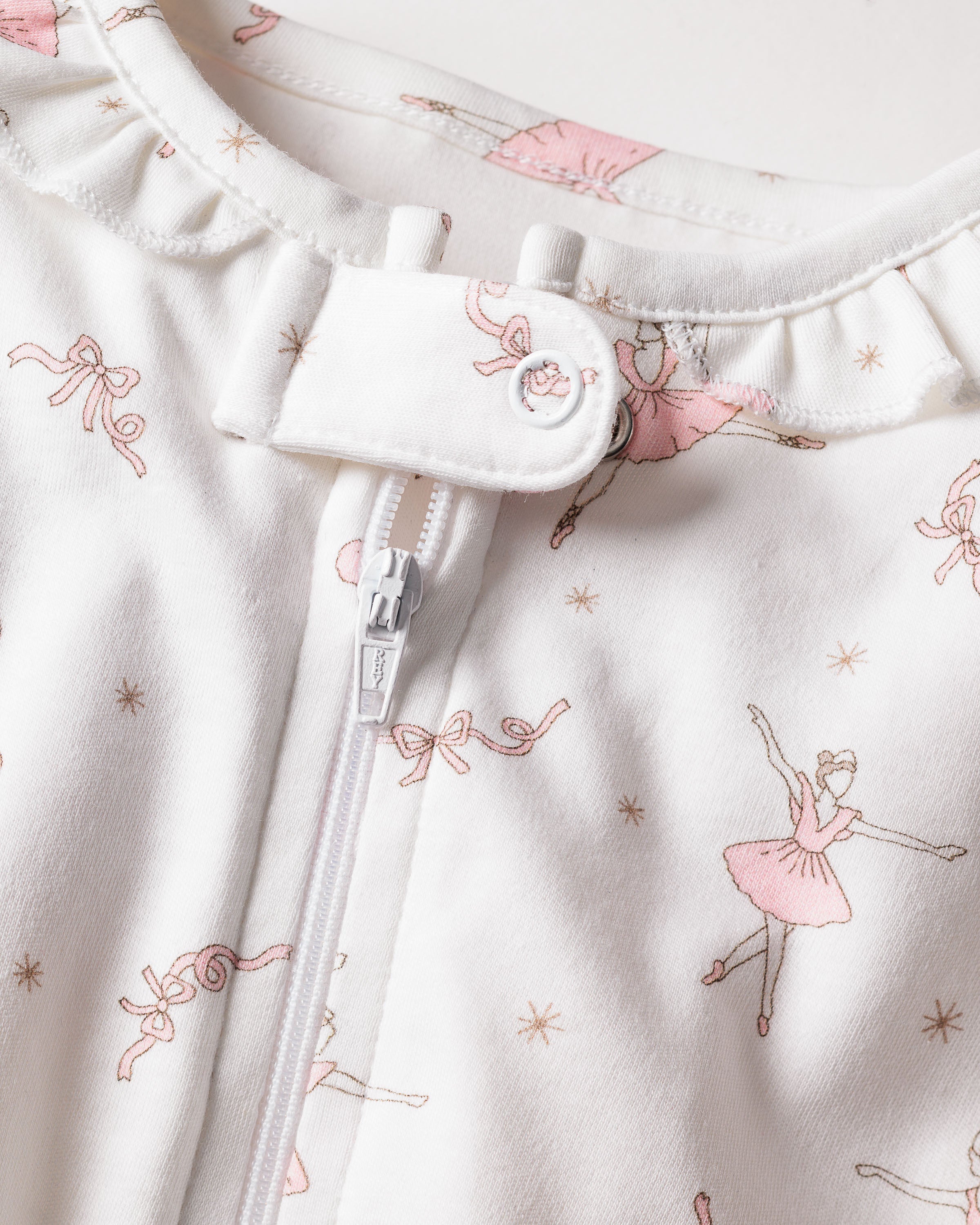 The Babys Pima Romper in Sugar Plum Fairy by Petite Plume showcases a white Pima cotton fabric with pink ballerina patterns, ribbons, and stars. It features a zipper and a buttoned neckline, creating elegant sleepwear.