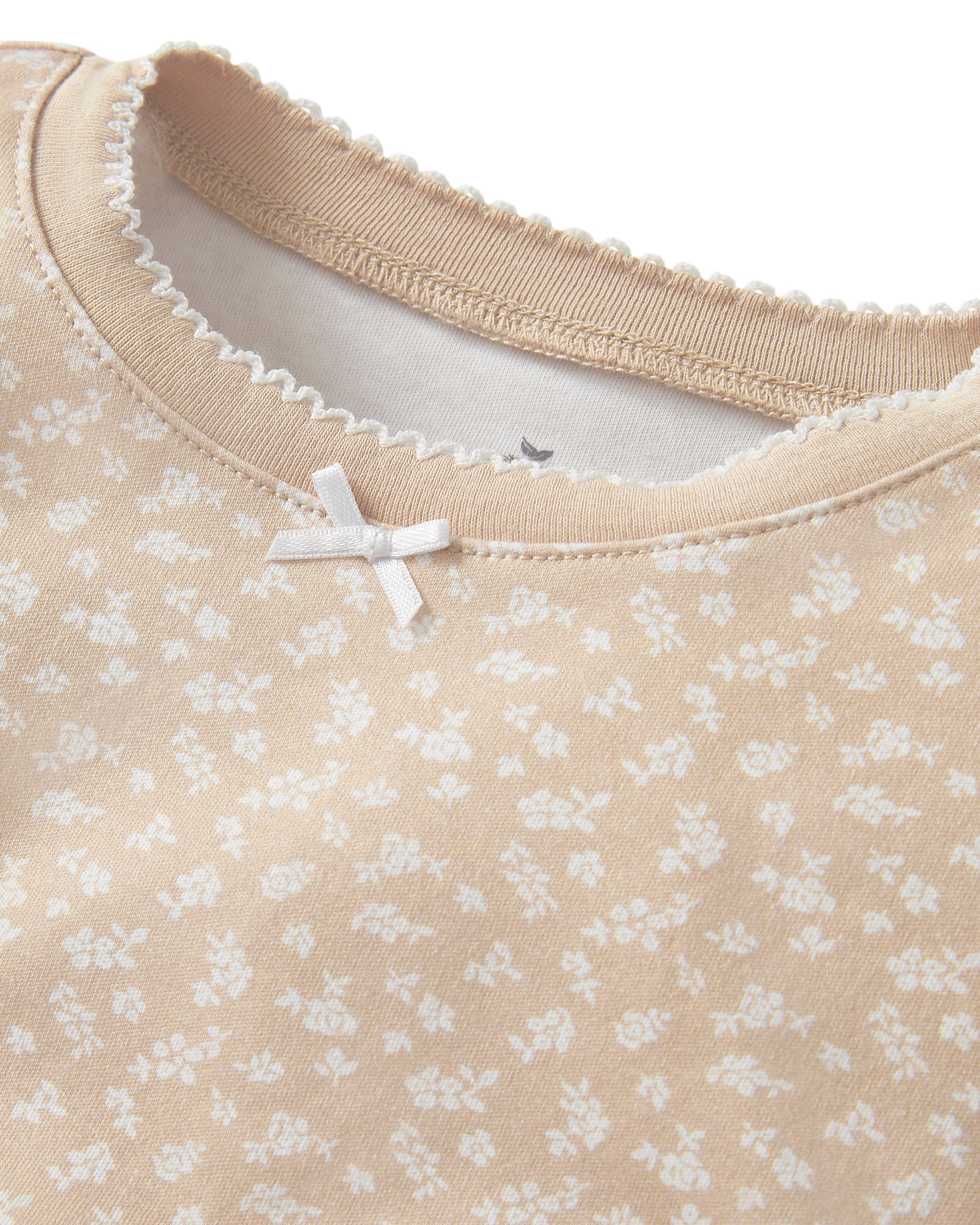 The Kid's Pima Snug Fit Short Set in Ditsy Waltz Camel is a beige, short-sleeve pajama set for kids with a subtle white floral pattern, featuring a top with a bow at the neckline and matching elastic-waist shorts.