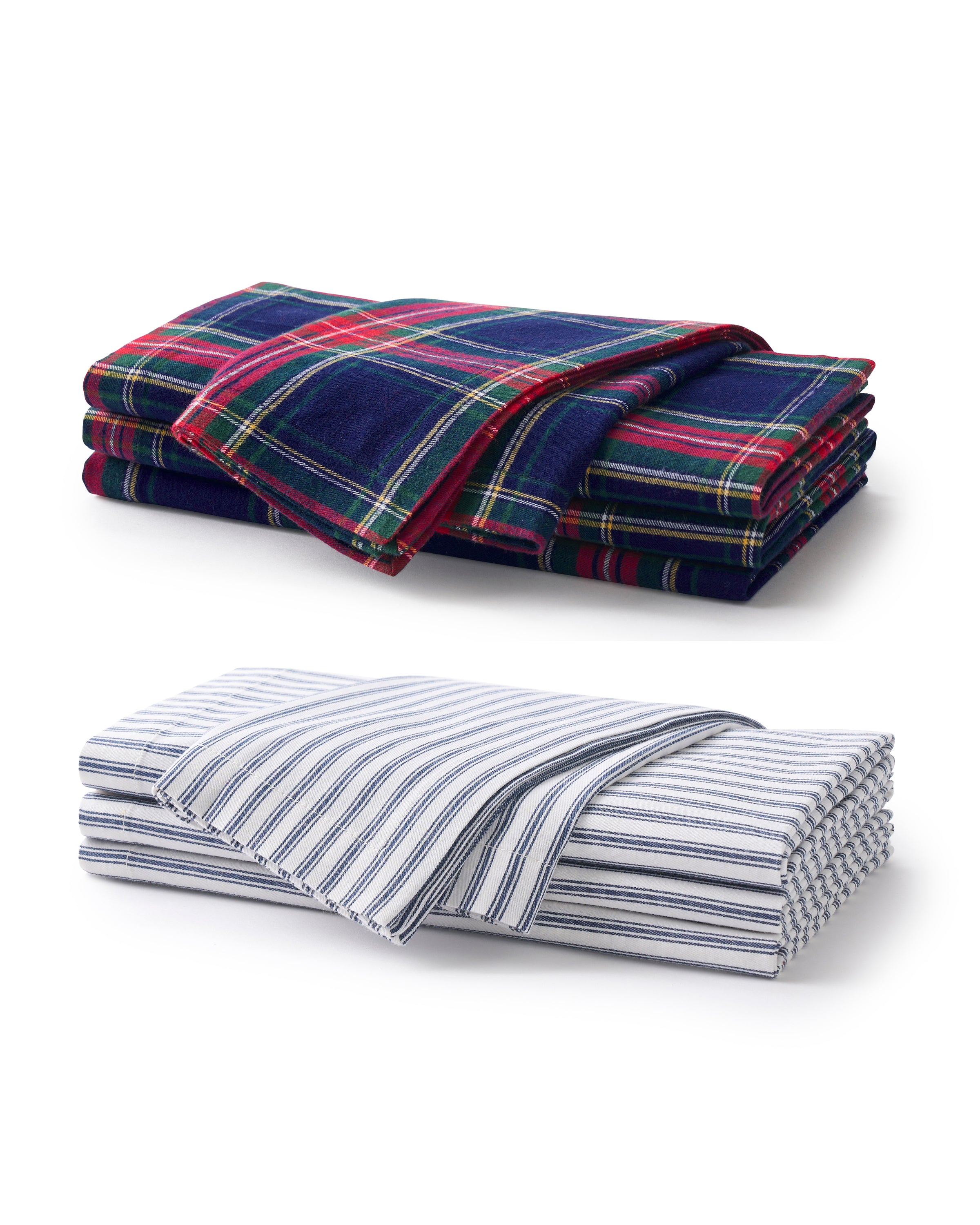 Two sets of Signature Twill Napkins—one in Windsor Tartan (dark blue, red, and green plaid) and one in Navy French Ticking (white with thin blue stripes)—are neatly stacked on a white surface.