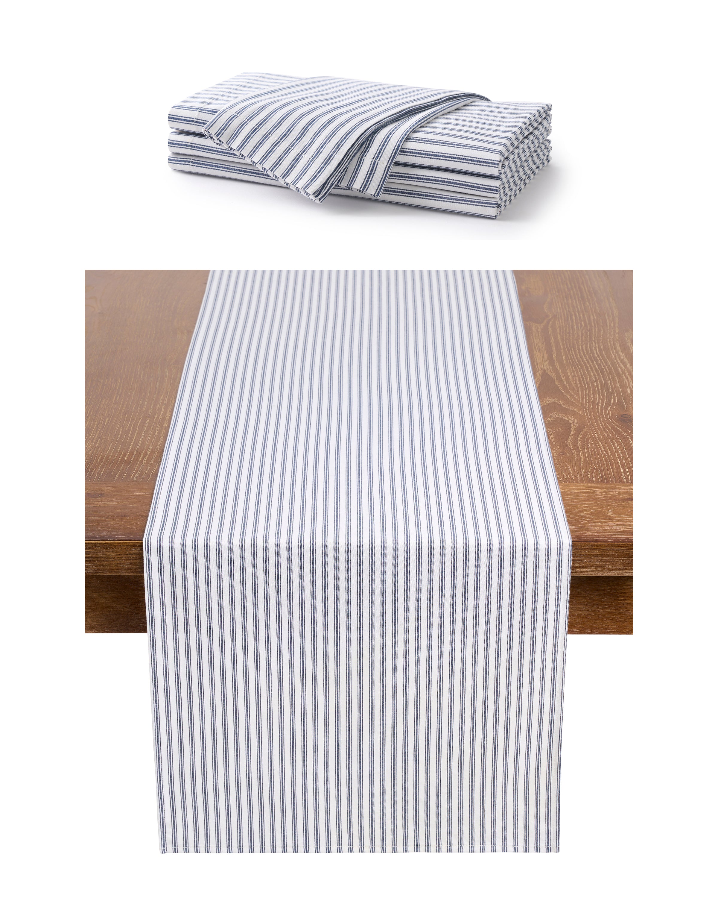 A stack of Petite Plumes Signature Twill Table Set in Navy French Ticking is neatly folded, highlighting the blue and white stripes. One 100% cotton runner is laid across a wooden table to showcase its design.