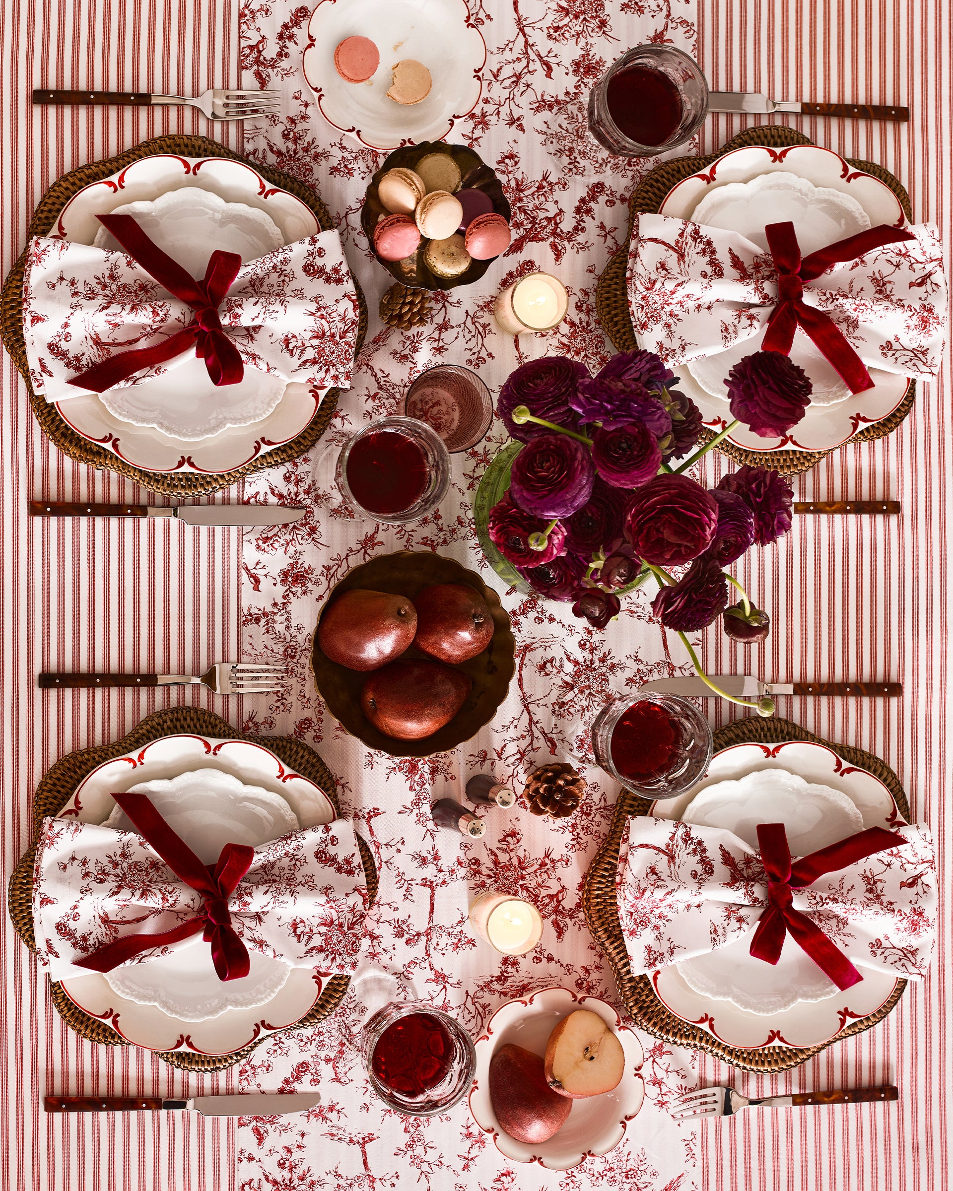 A wooden table with a Signature Twill Tablecloth in Antique Red Ticking by Petite Plume partially draped over it. The cloth showcases its crisp linear pattern and is enhanced by carved legs, offering an elegant touch for a festive tablescape that highlights its simple yet sophisticated design.
