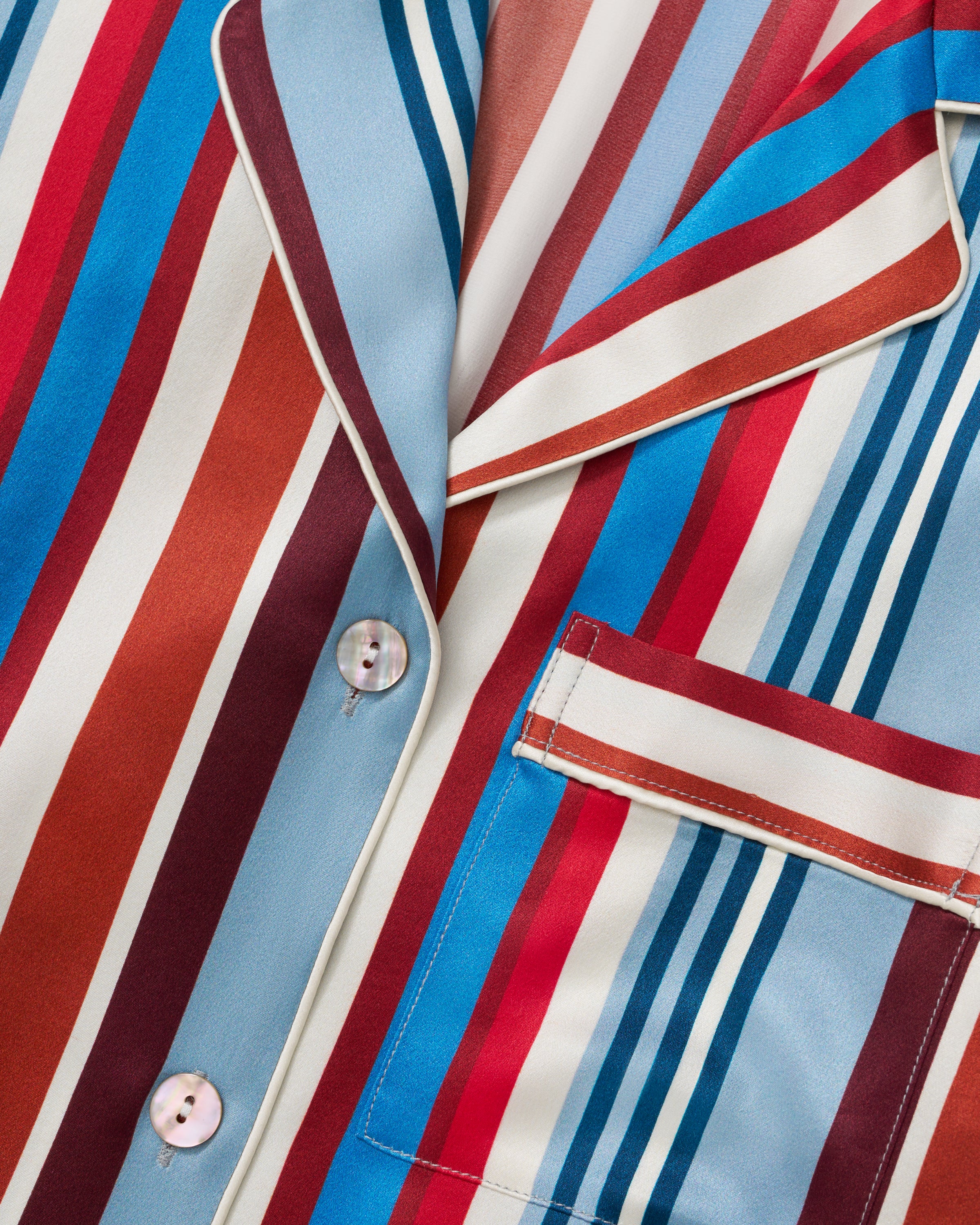 The Women's Silk Pajama Set in Discovery Stripe features long-sleeve, button-up top and matching pants with bold red, blue, brown, and white vertical stripes on smooth silk, displayed on a white background.