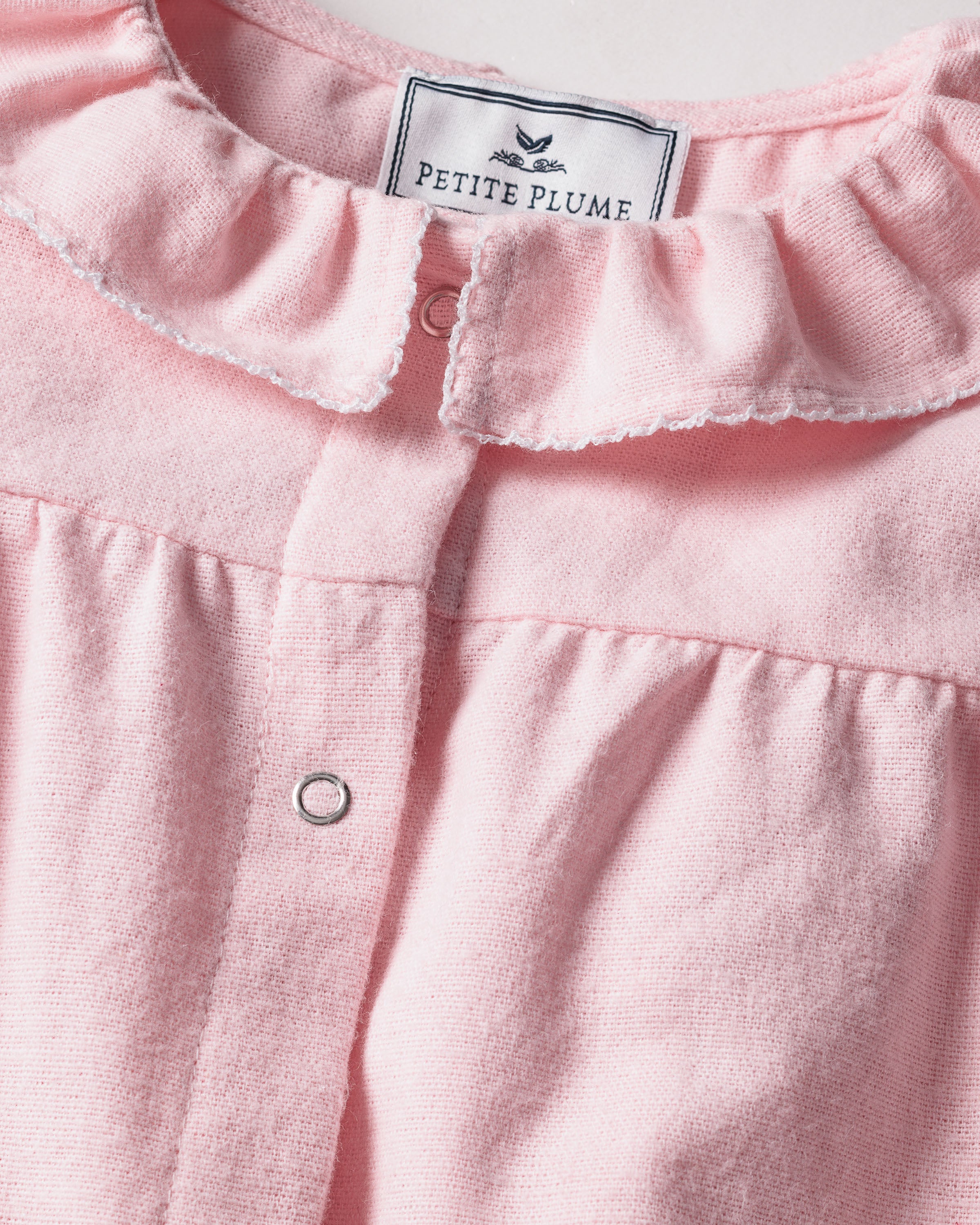 Close-up of the Babys Flannel Madeline Romper in Pink by Petite Plume, featuring a small white label. The ultra-soft brushed flannel adds to its comfort, complemented by front button details—ideal for childrens sleepwear.