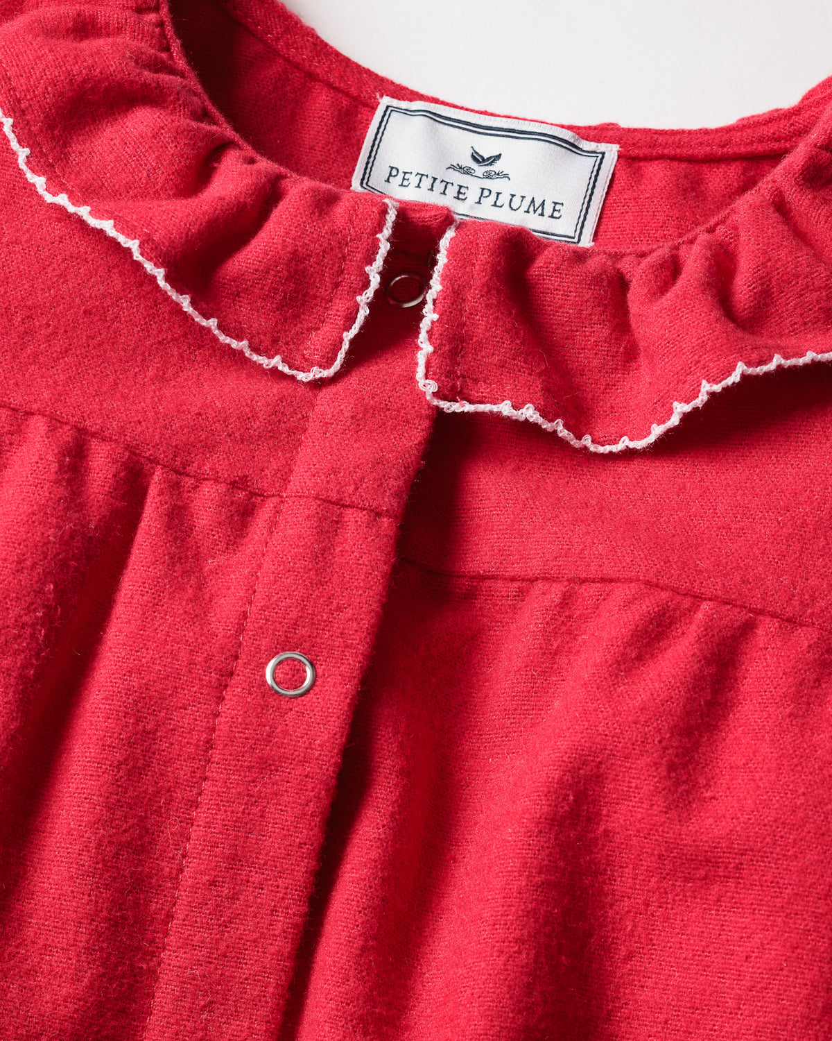 Close-up of the Petite Plume Babys Flannel Madeline Romper in Red, showcasing a ruffled collar with white trim and buttoned front. Crafted from chemical-free, flame-retardant fabric for childrens safety, this sleepwear has an inner label reading Petite Plume.