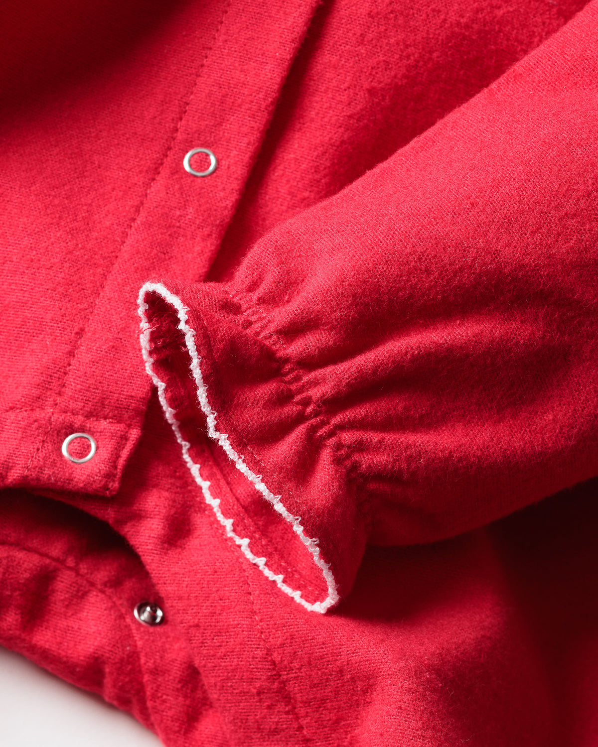 Close-up of Petite Plumes Babys Flannel Madeline Romper in red, ideal for childrens sleepwear, highlighting a sleeve with elastic gather and decorative white stitching. The soft fabric includes metallic snap buttons on the body for comfort and ease.