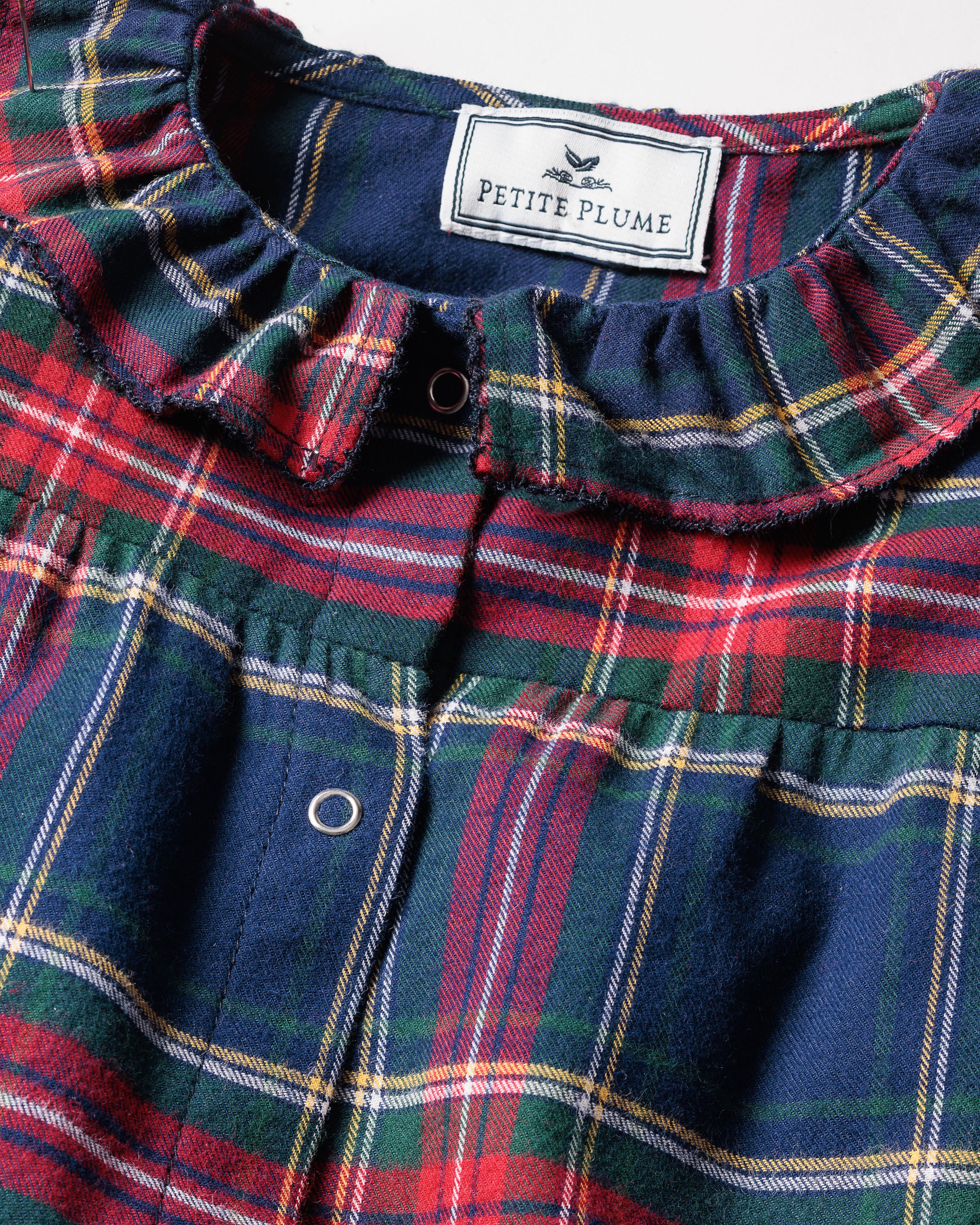 Close-up of the Babys Brushed Cotton Madeline Romper in Windsor Tartan by Petite Plume, featuring a plaid design with red, green, and blue colors, a ruffled collar, and snap buttons. The label ensures it is chemical-free for comfort and peace of mind.