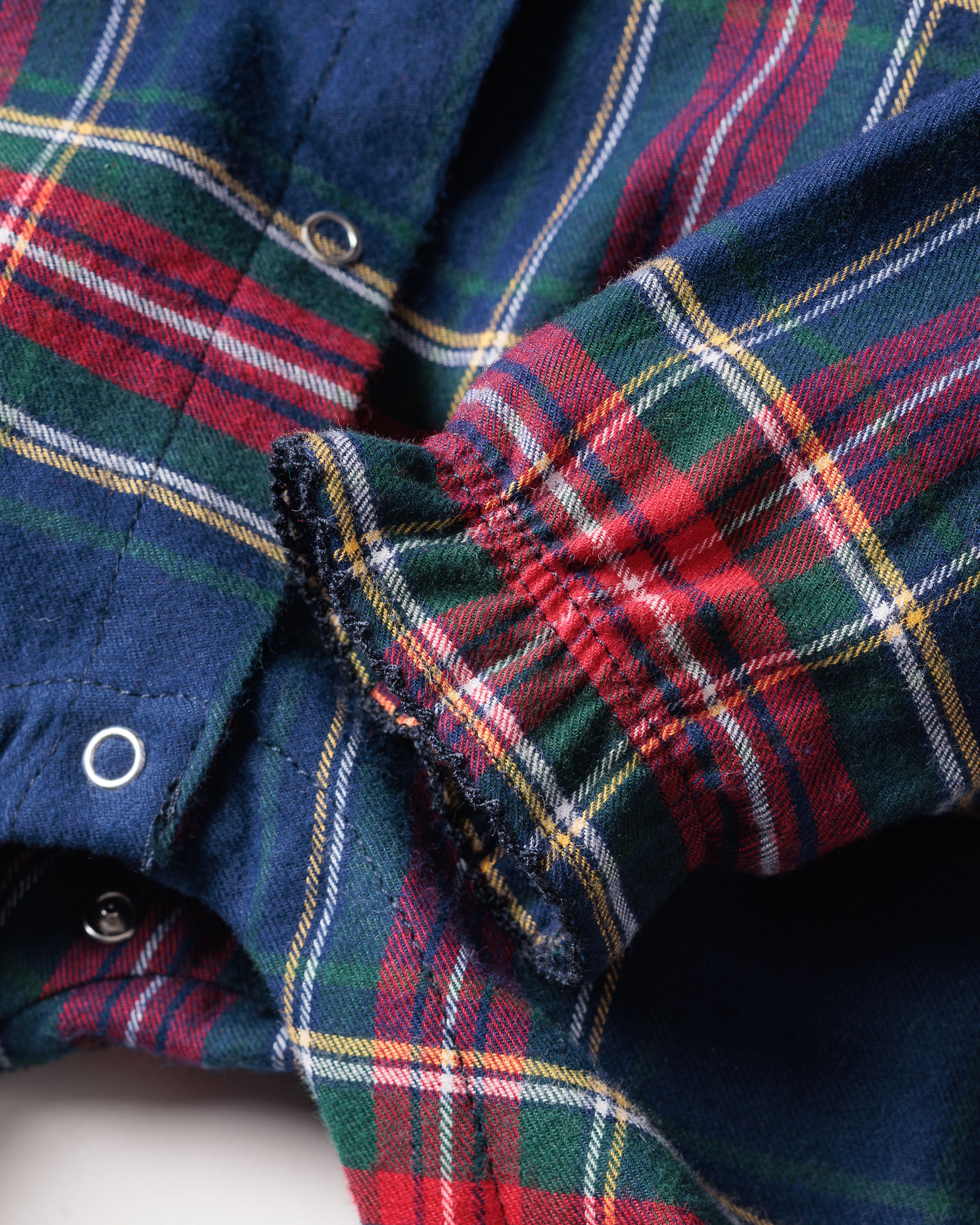 A close-up of the Petite Plume Babys Brushed Cotton Madeline Romper in Windsor Tartan shows red, green, blue, and yellow patterns with slightly frayed fabric near the cuff, reminiscent of well-loved childrens sleepwear. Casually arranged to highlight the texture and button details.