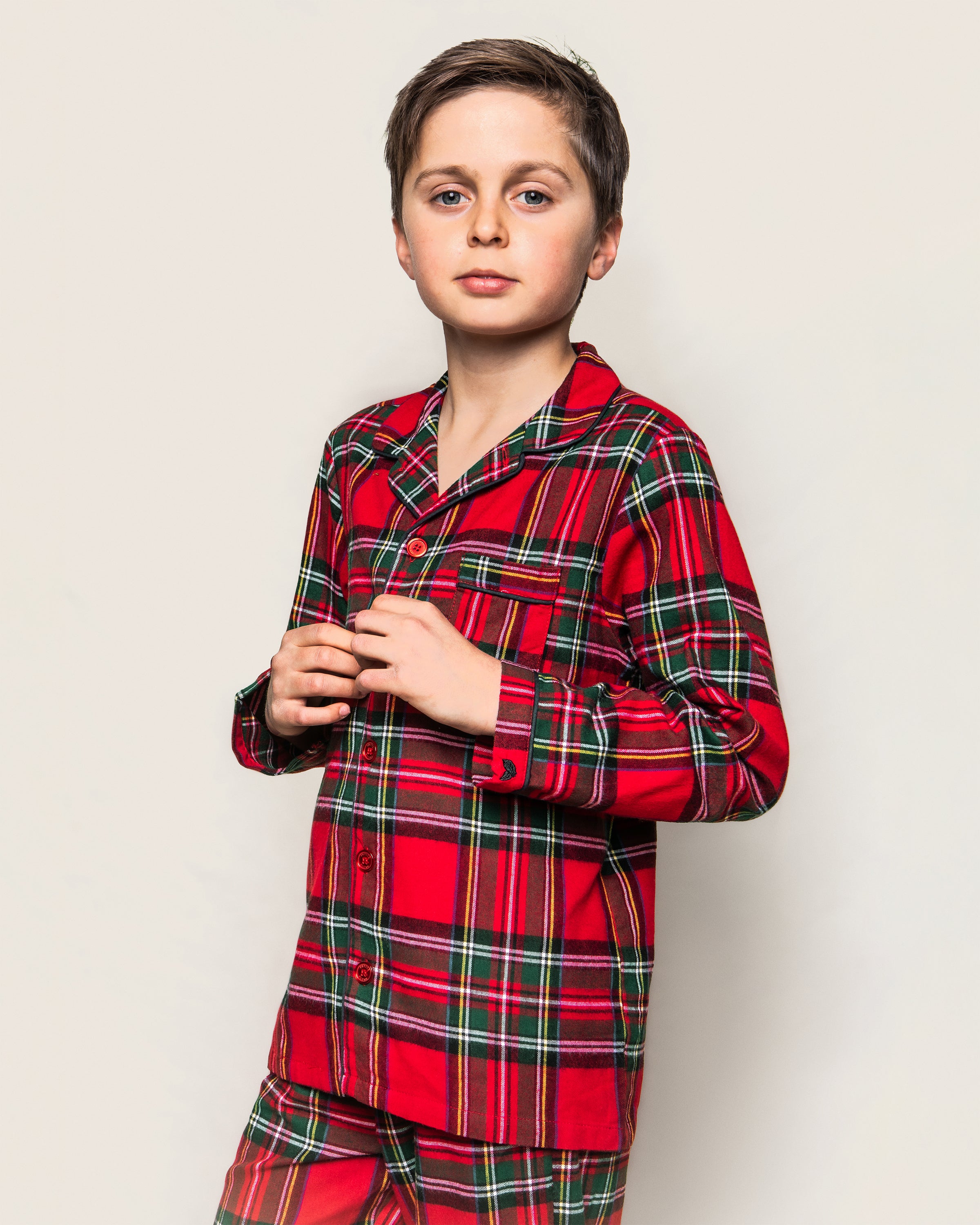 A confident young person wears Petite Plumes Kids Brushed Cotton Pajama Set in Imperial Tartan. The yarn-dyed cotton top has a button-up front and chest pocket, set against a plain, light-colored background.