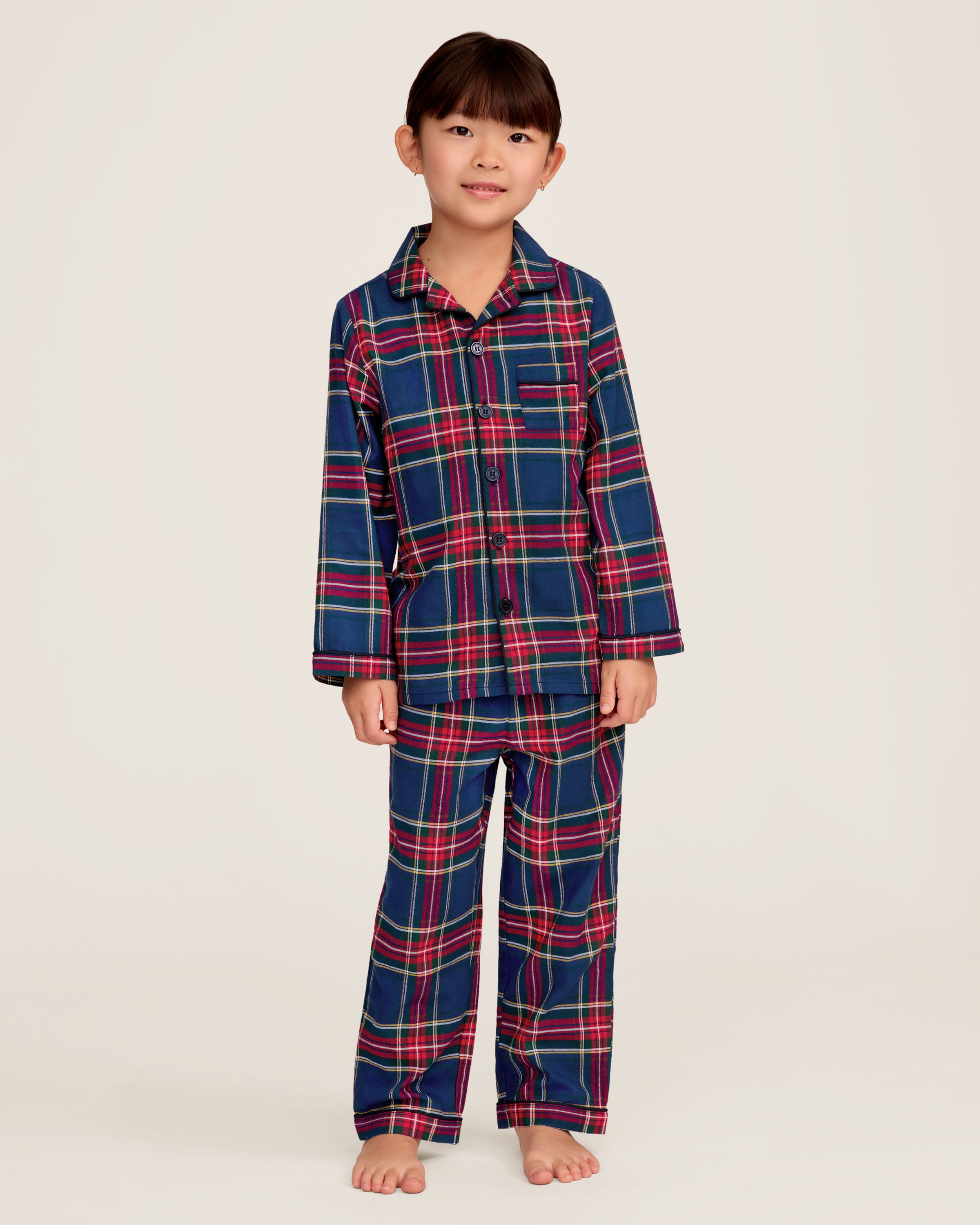 Close-up of a lavish Kids Brushed Cotton Pajama Set in Windsor Tartan by Petite Plume, showcasing red, blue, green, and yellow intersecting stripes forming squares and rectangles. A visible button and seam complete this classic pajama look.