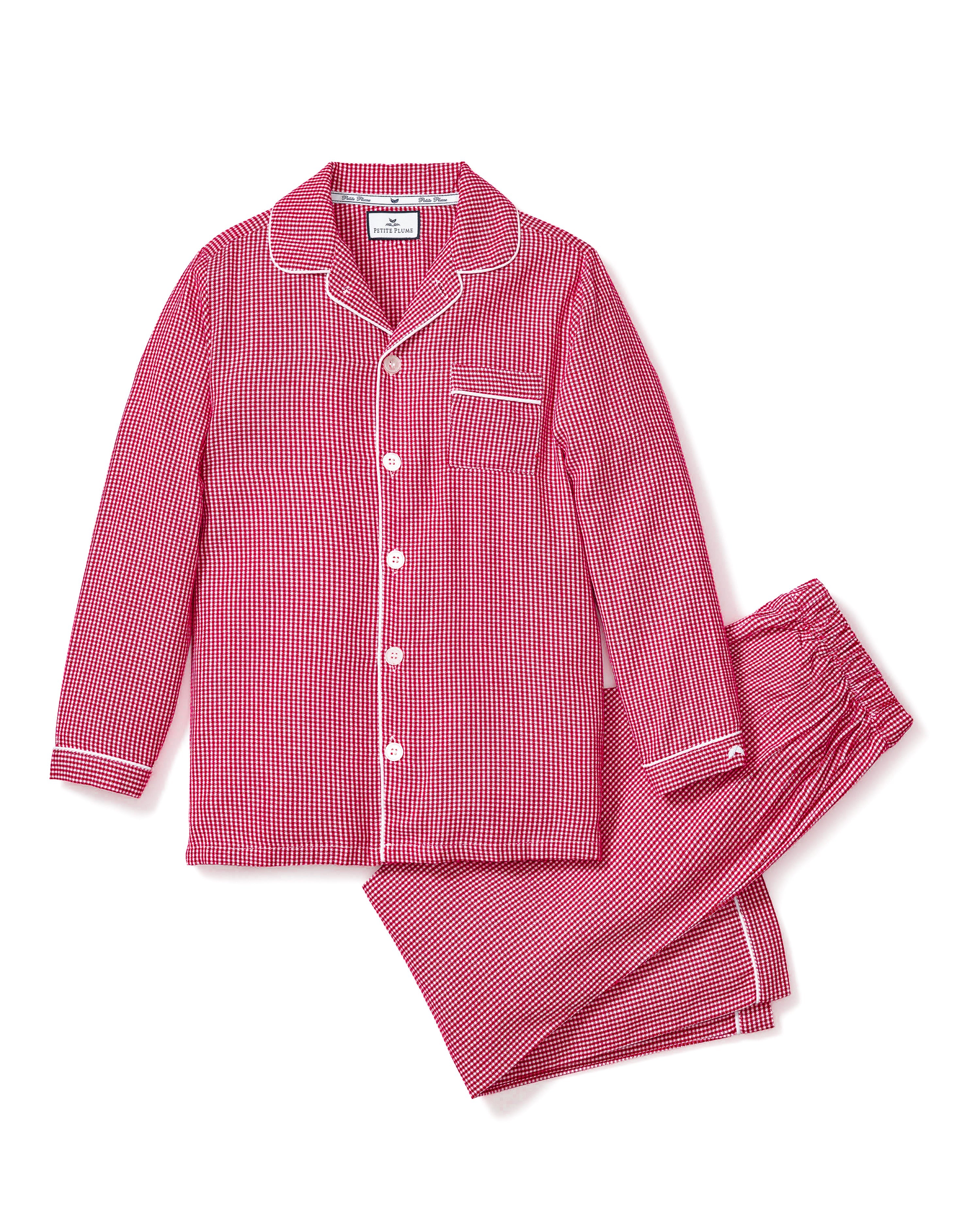 The Kids Flannel Pajama Set in Red Mini Gingham by Petite Plume offers luxurious sleepwear with a classic design, featuring red and white gingham. The set includes a long-sleeved button-up shirt with a chest pocket and matching pants with an elastic waistband for added comfort.