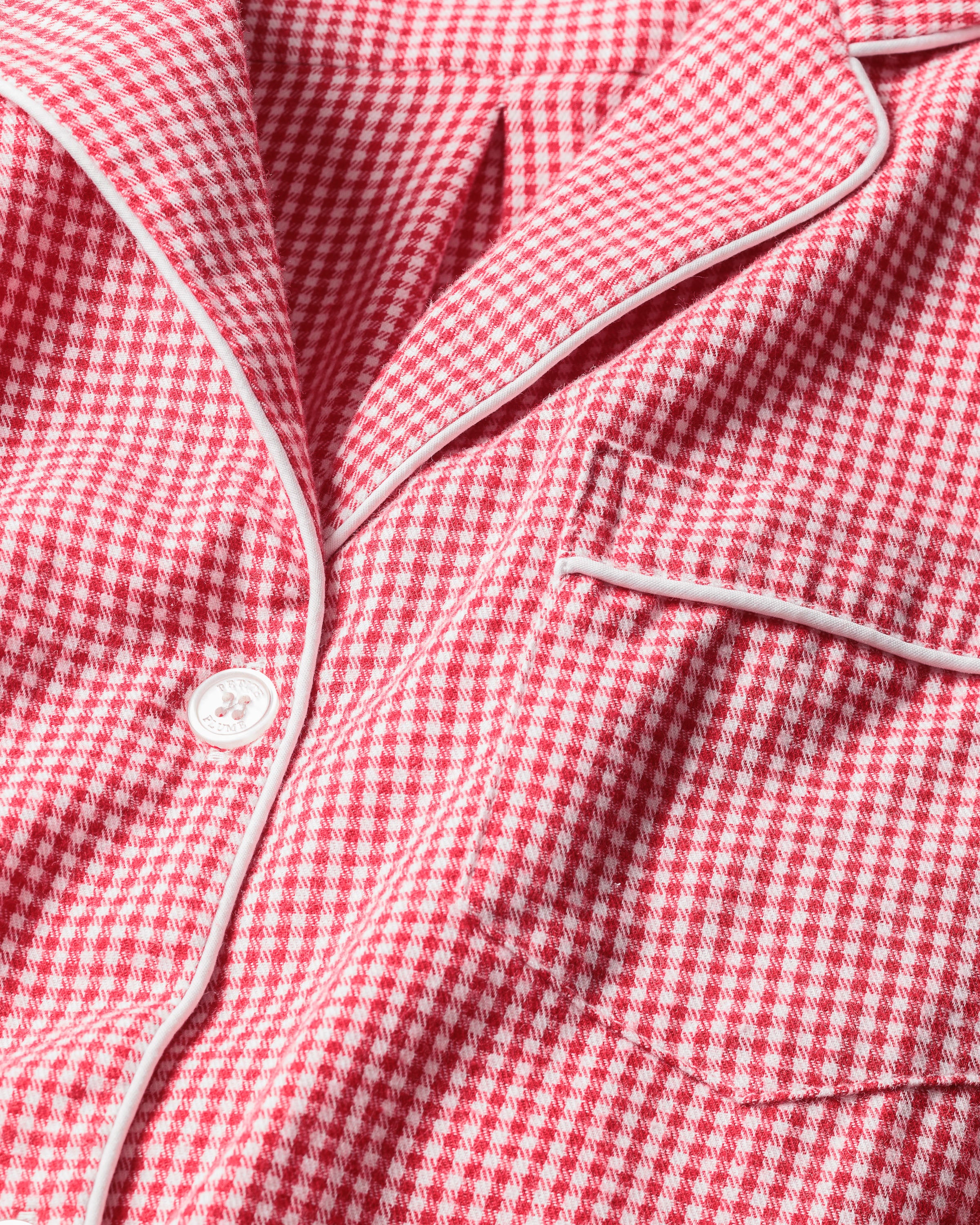 Close-up of Petite Plumes Kids Flannel Pajama Set in Red Mini Gingham, showcasing a button-down style with elegant white piping. The classic gingham pattern is enhanced by a timeless pocket on the right side.