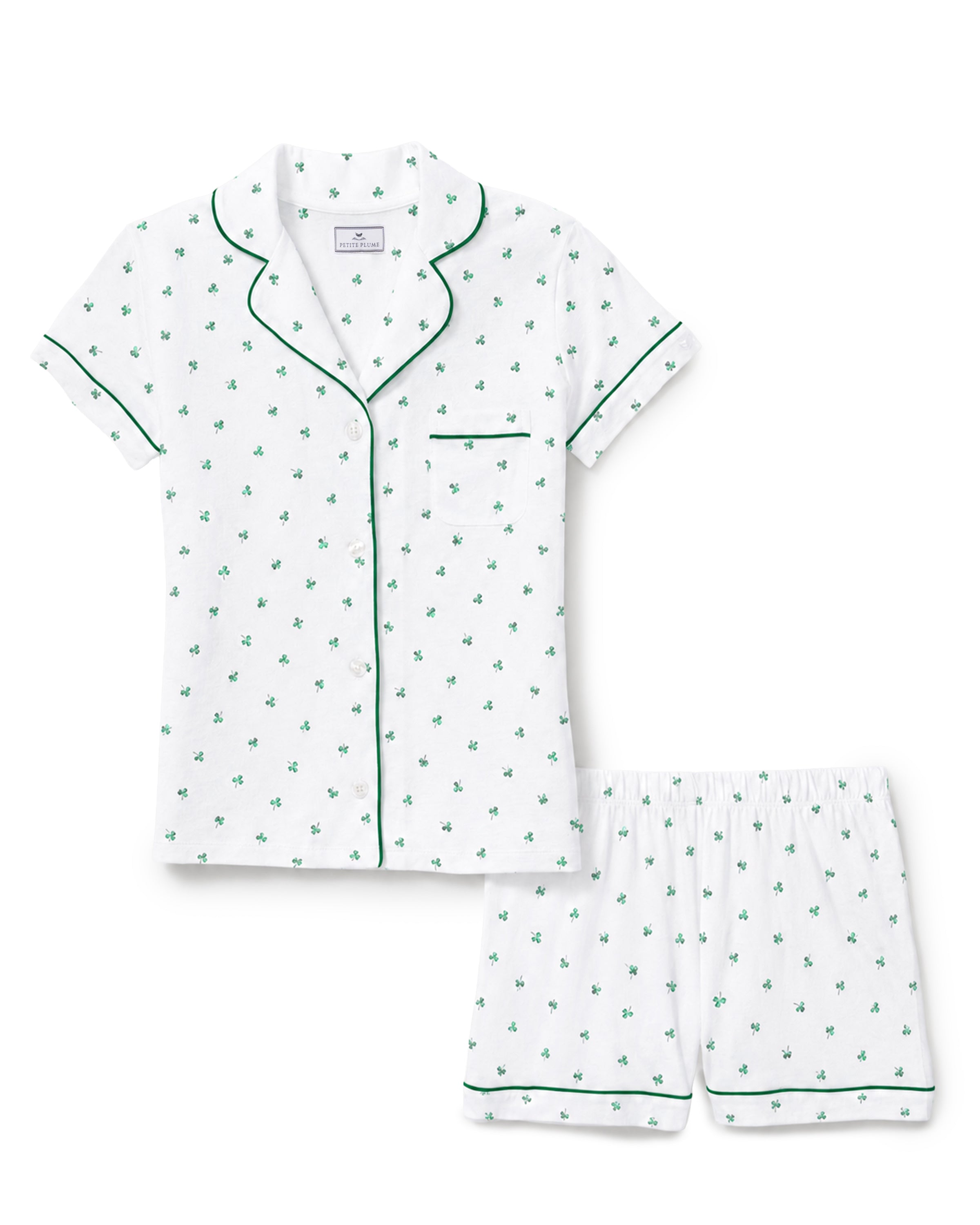 The Poppy Lightweight Pima Short Set in Shamrocks features a white short-sleeve pajama set with green piping and a small green shamrock print, including a button-up top with a chest pocket and matching shorts.