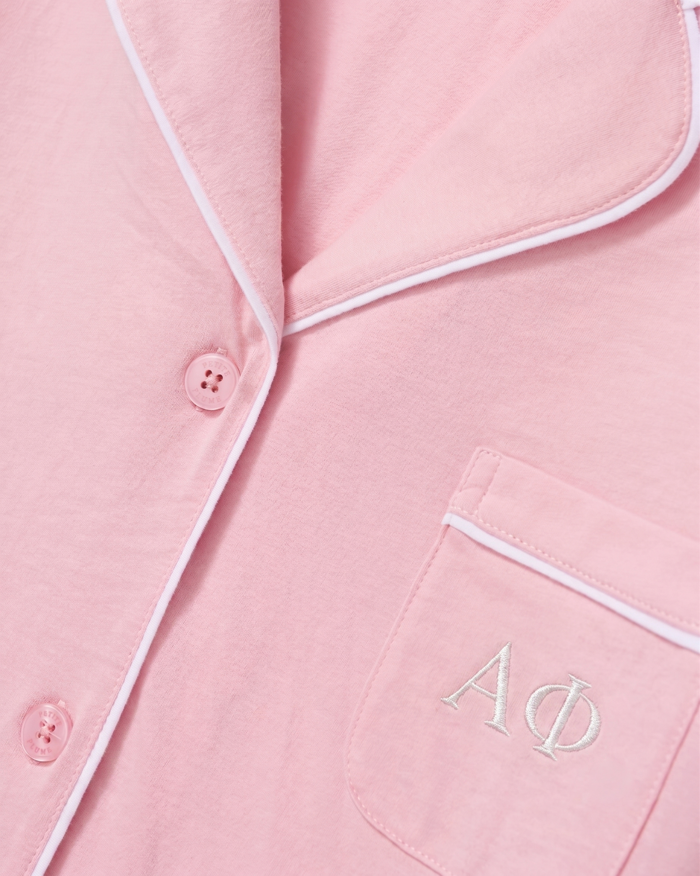 Close-up of the Greek Embroidered Poppy Lightweight Pima Short Set in Pink, featuring a light pink pajama top with white piping, pink buttons, and white embroidered Greek letters ΑΦ on the chest pocket.