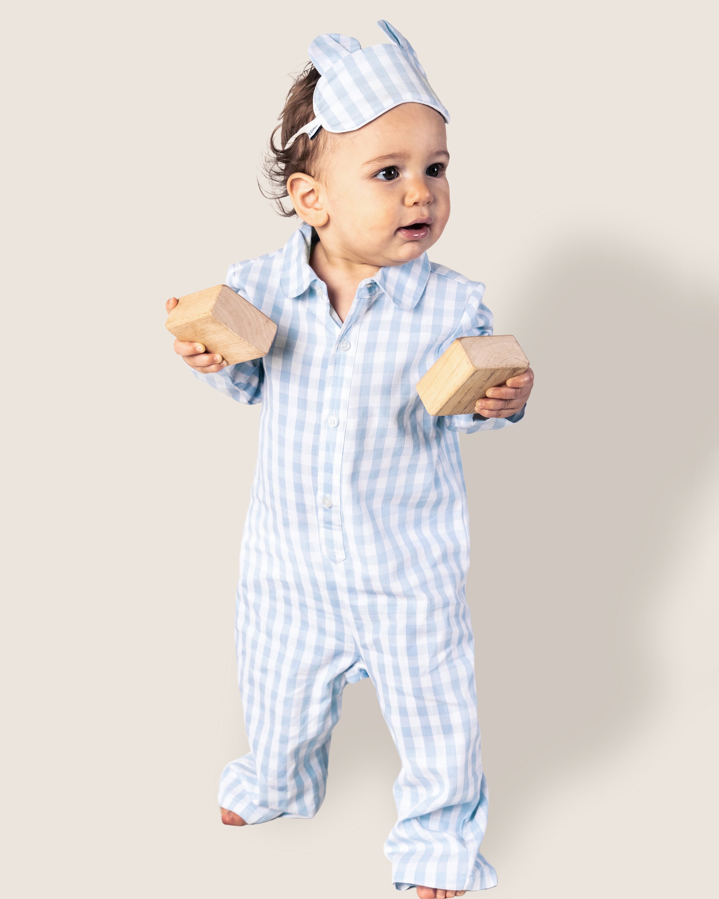 The Baby's Twill Classic Romper in Light Blue Gingham features long sleeves, full-length design, a collar, white front buttons, and snap closures along the legs in a light blue and white gingham pattern.