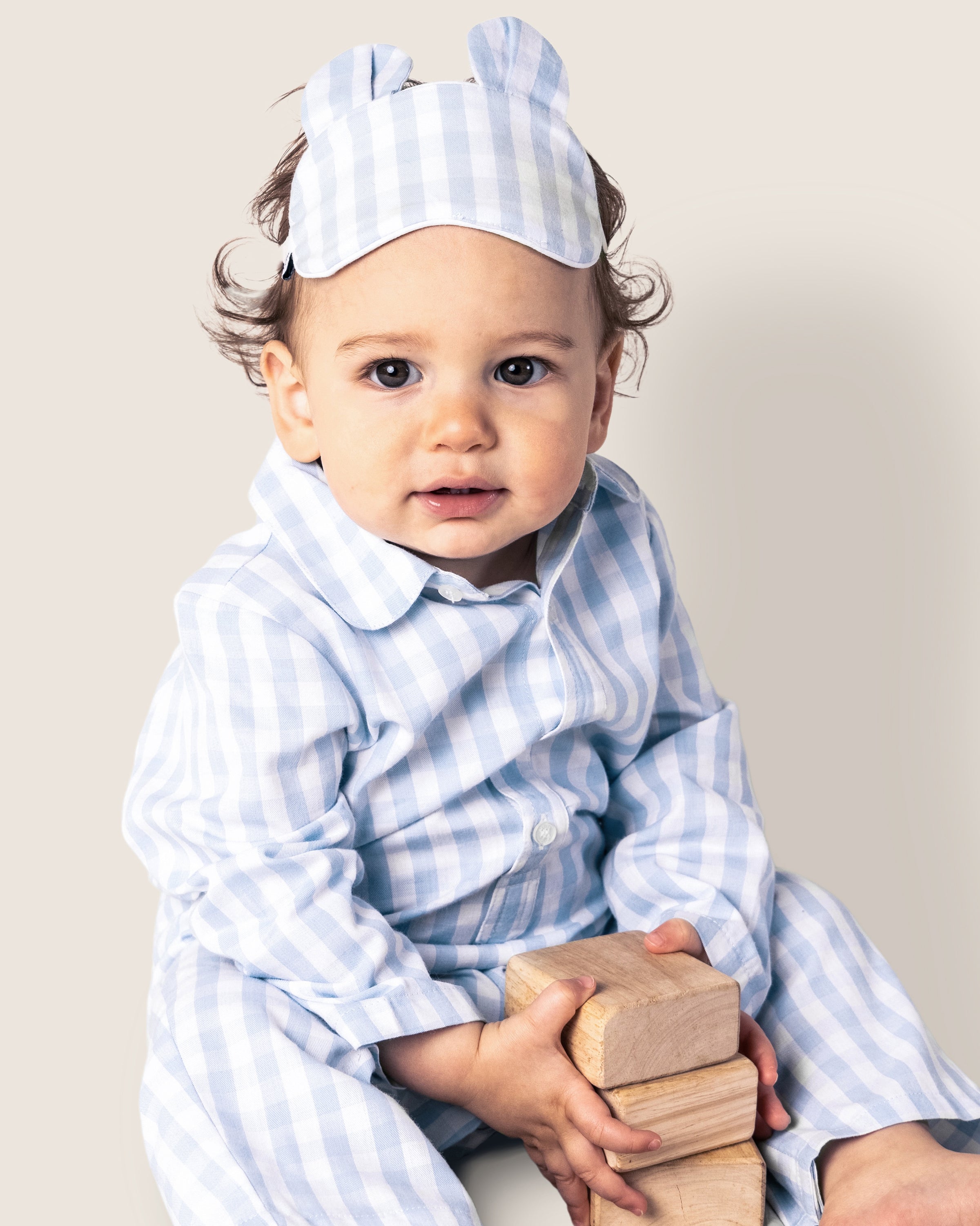 The Baby's Twill Classic Romper in Light Blue Gingham features long sleeves, full-length design, a collar, white front buttons, and snap closures along the legs in a light blue and white gingham pattern.