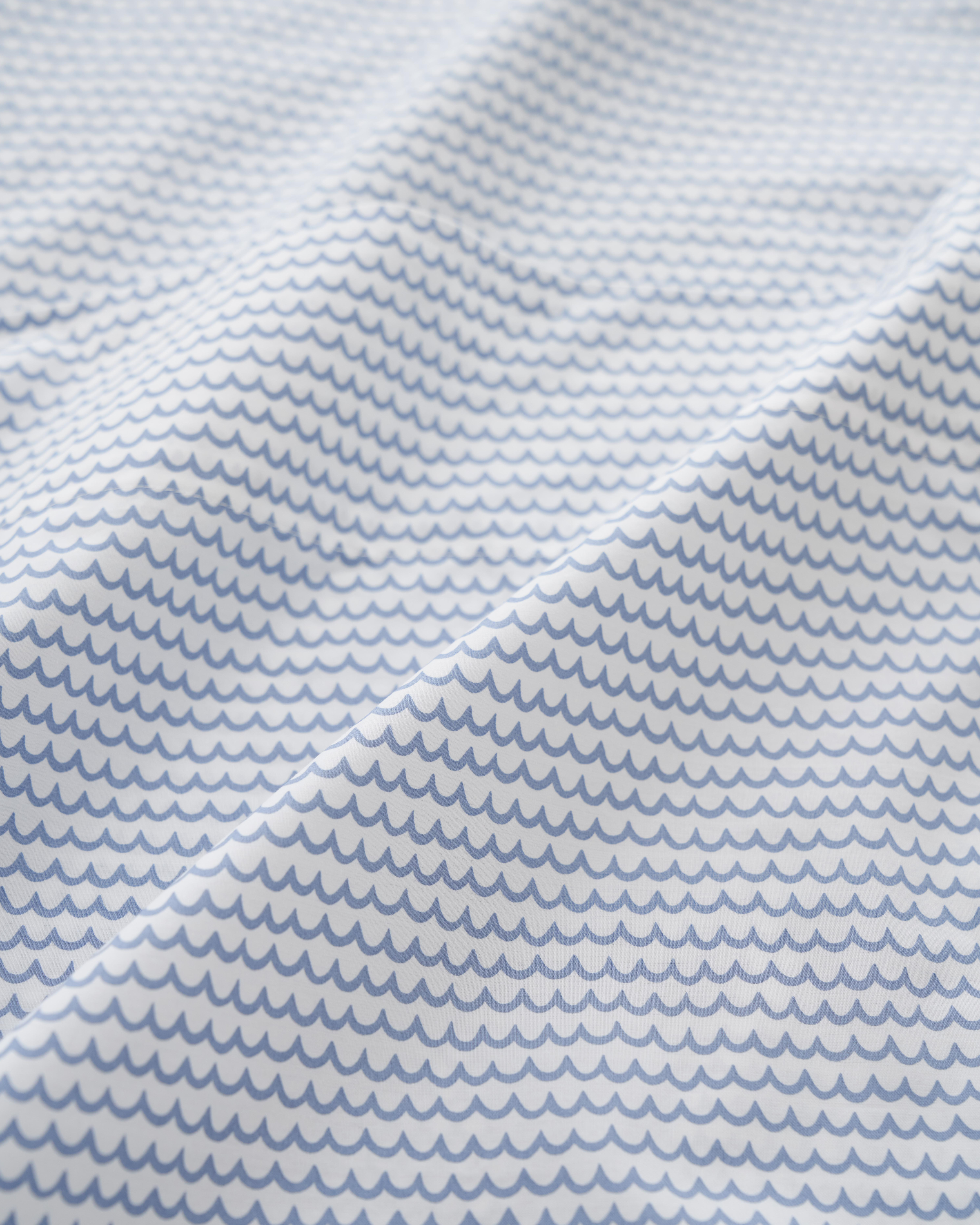 The Luxe Premium Cotton La Mer Bed Sheets by Petite Plume feature a pattern of small, evenly spaced blue scallops on a white background, creating a wave-like effect. The breathable cotton fabric offers a slightly creased texture for added depth and elegance.