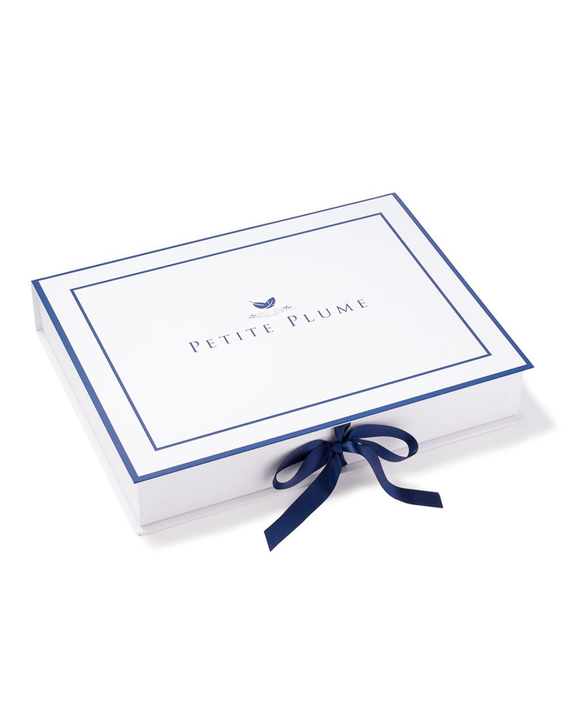 A rectangular white box with a blue border reads Petite Plume on the lid. A navy satin ribbon, echoing our Womens Silk Long Robe in Navy, is tied into a bow on the right side.