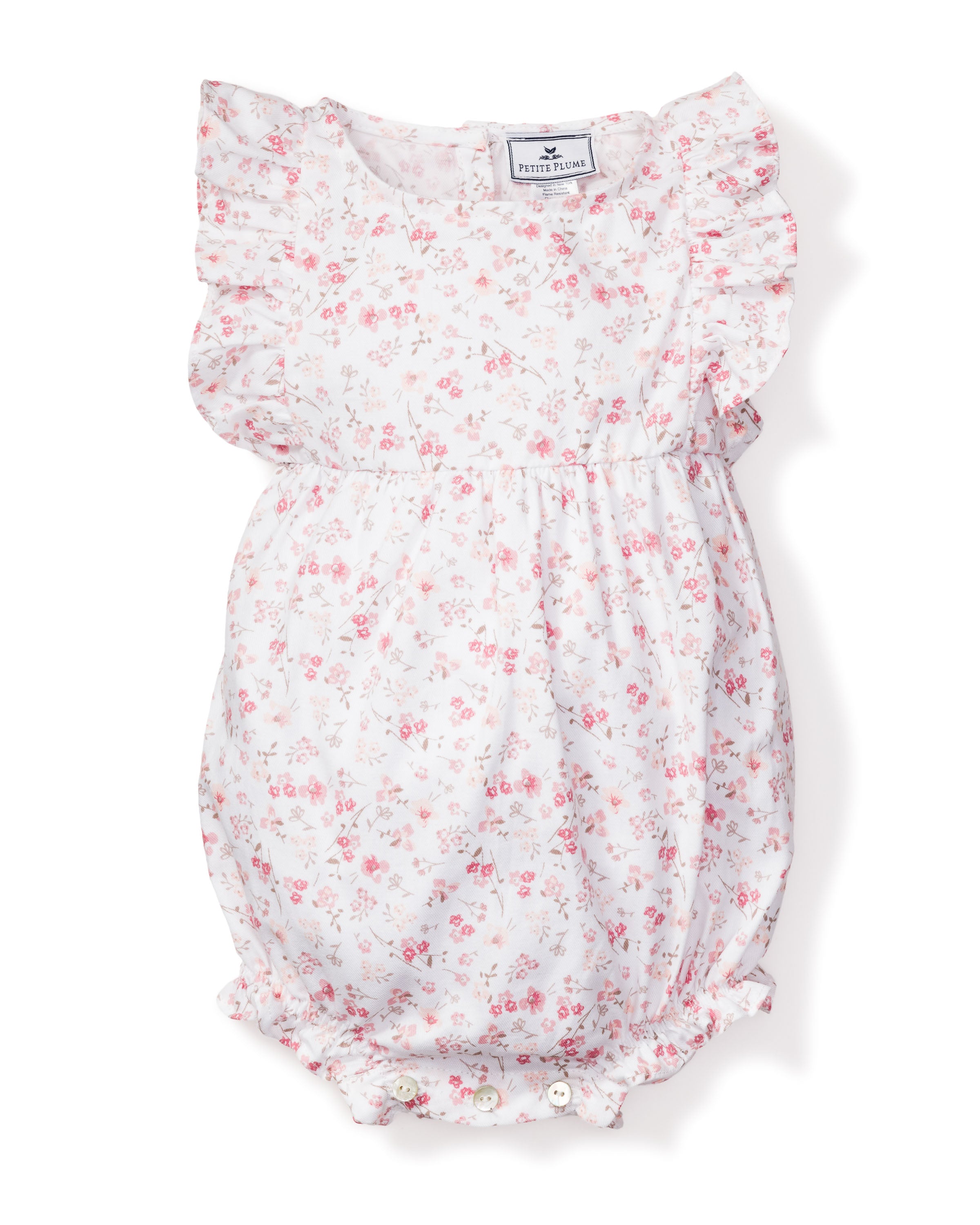 The Babys Twill Ruffled Romper in Dorset Floral by Petite Plume is a charming Victorian-inspired piece featuring pink flowers on white with ruffled sleeves, a gathered waist, and visible bottom buttons for classic elegance and modern comfort.