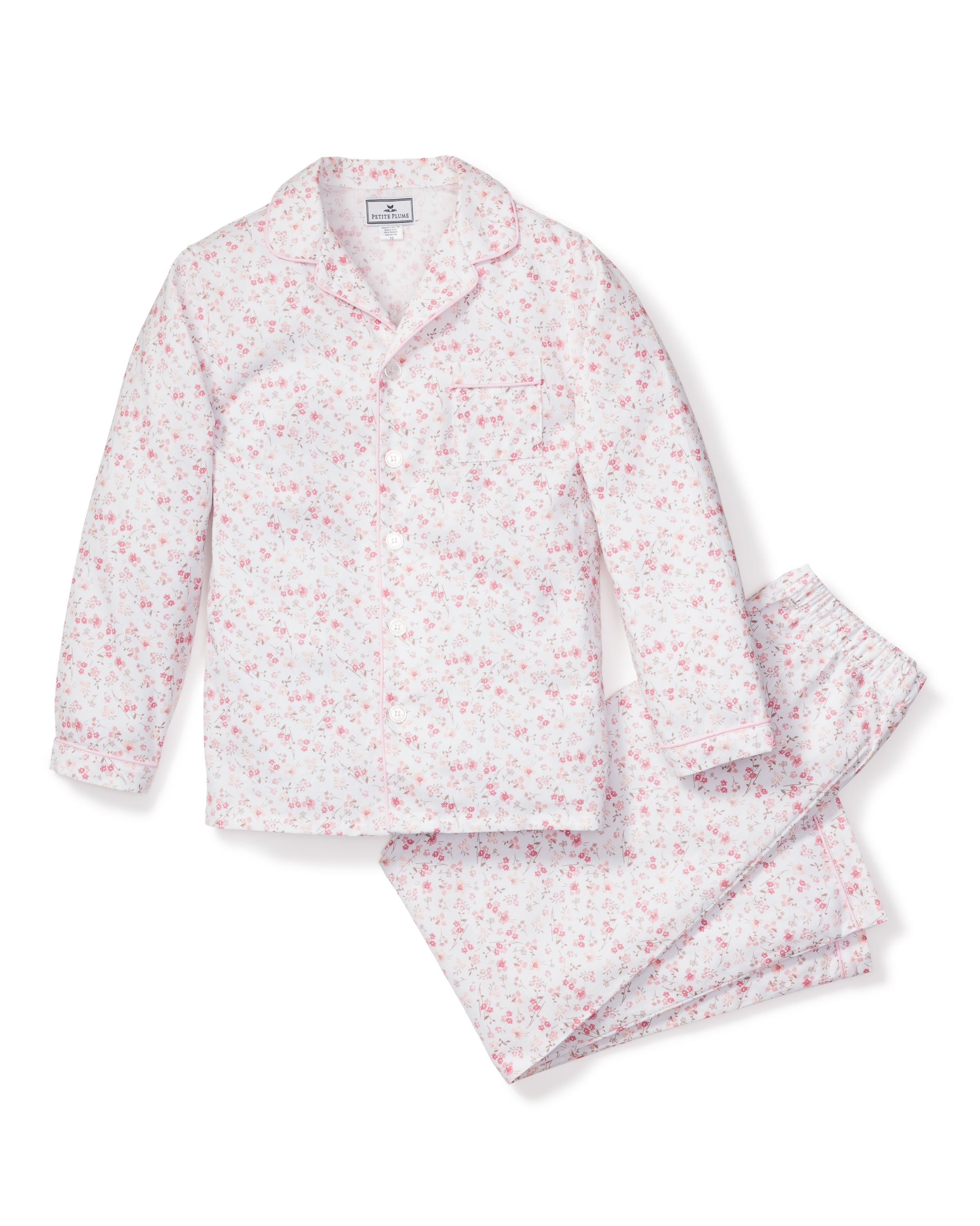 The Kids Twill Pajama Set in Dorset Floral by Petite Plume is a luxurious white set with pink and red floral patterns. Made of soft cotton, it includes a long-sleeve button-up top with a left pocket and matching pants, designed for ultimate comfort.