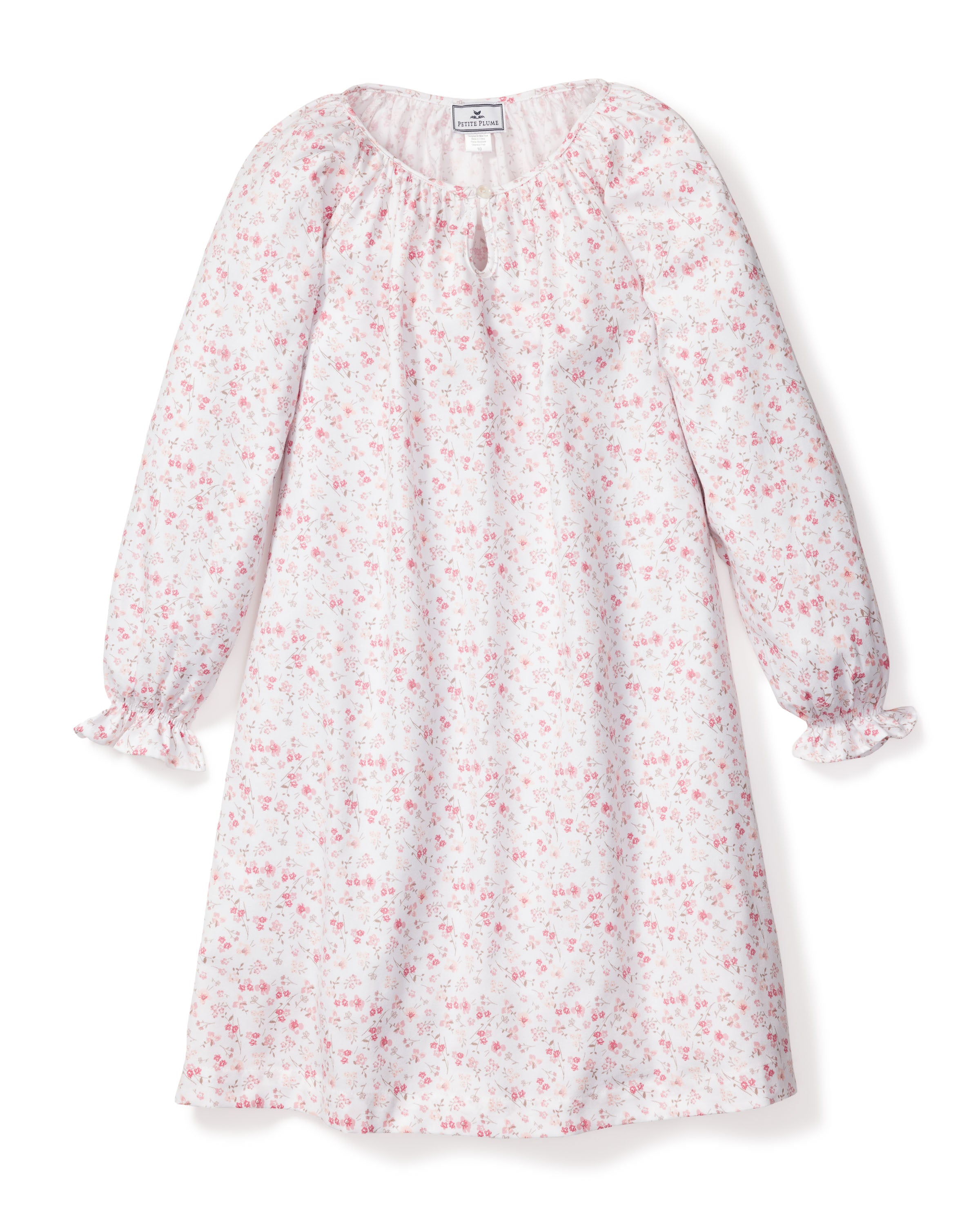 The Girls Twill Delphine Nightgown in Dorset Floral by Petite Plume is a luxurious sleepwear piece with a white base and delicate pink floral design. It features a ruffled collar with keyhole opening and ruffled cuffs, made from flame-retardant, lightweight fiber for comfort and safety.