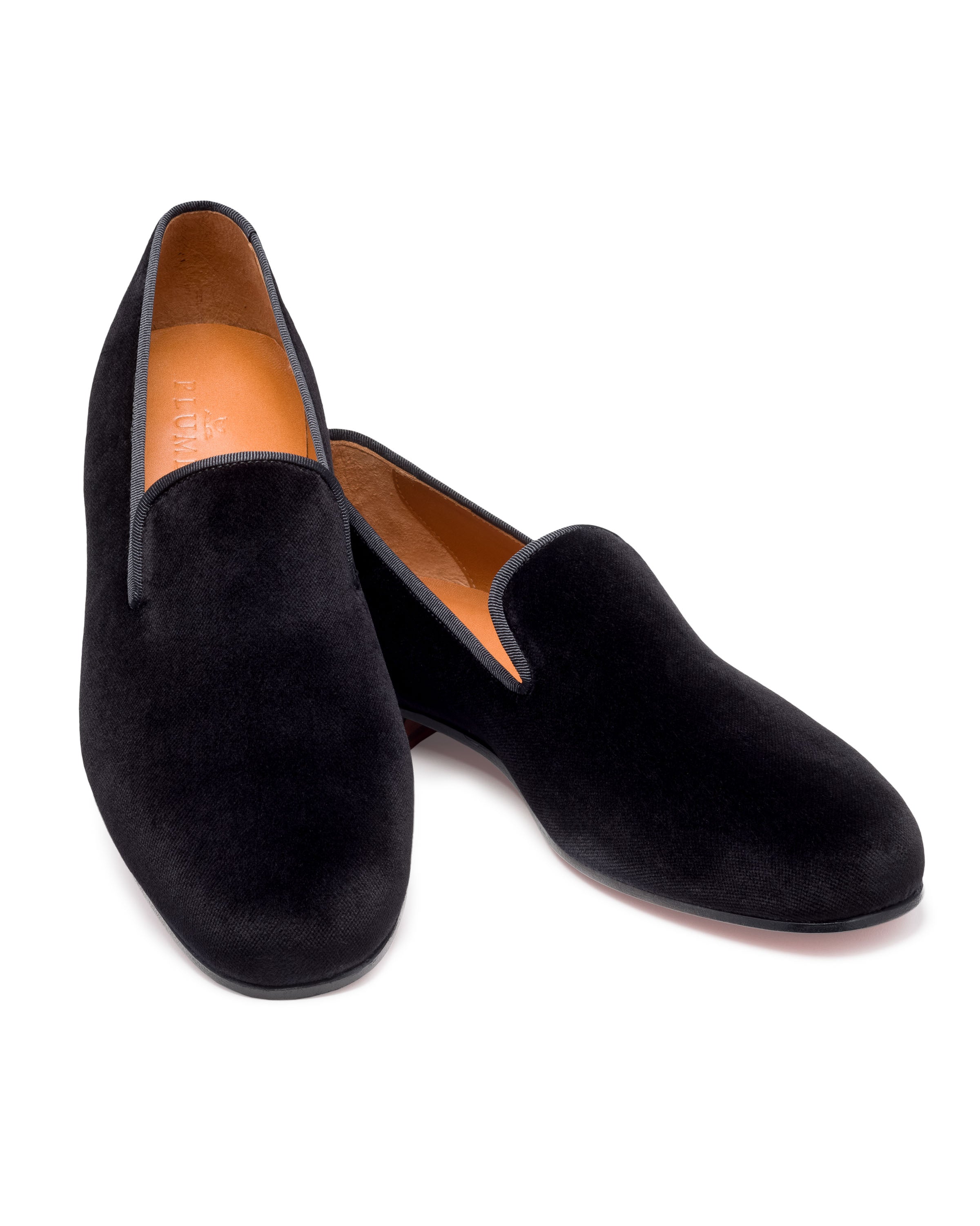 The Mens Hamptons Loafer in Black by Petite Plume is a pair of luxurious velvet loafers with a minimalist design and tan-colored insoles. They exude sophistication, making them perfect for pairing with mens pajamas for an elegant evening at home, pictured overlapped on a white background.