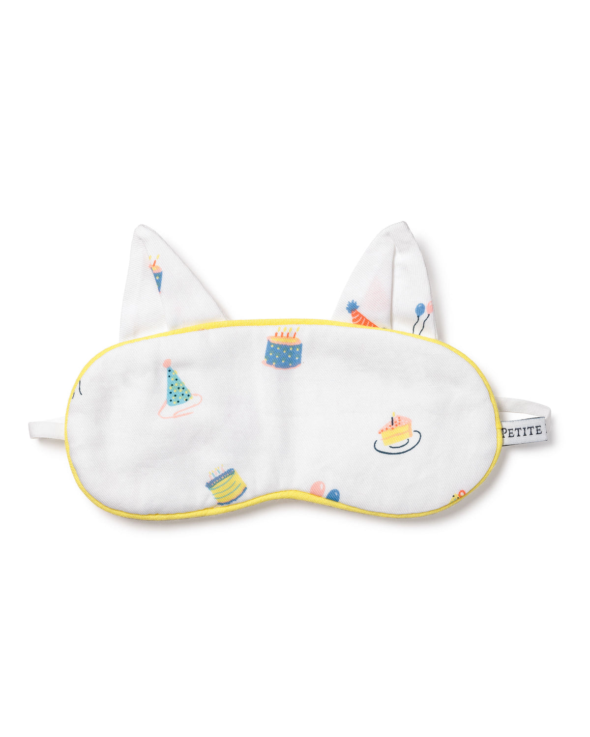 The Kids Twill Kitty Sleep Mask in Birthday Wishes by Petite Plume is a luxurious white eye mask with yellow trim, featuring colorful cake, party hat, and balloon illustrations. It includes two fabric ears, an elastic strap, and can be monogrammed for personalization.
