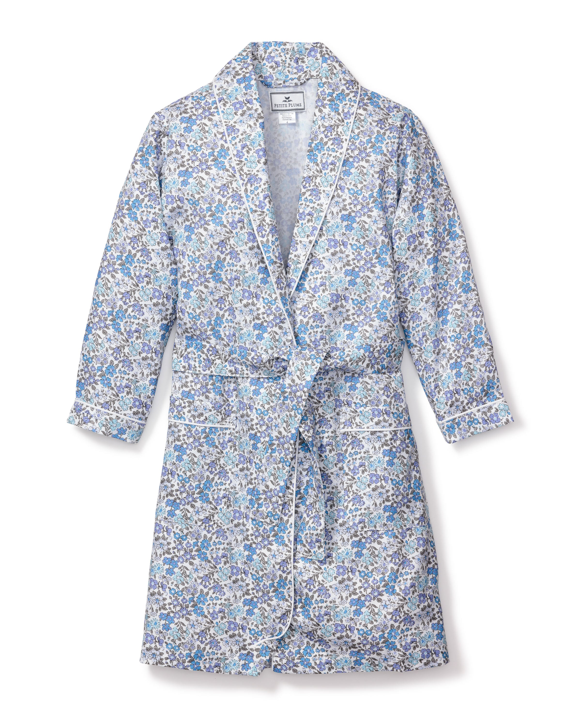 The Kids Twill Robe in Fleur DAzur by Petite Plume features a vintage-inspired floral print with blue, white, and gray flowers. Made from yarn-dyed cotton, it boasts long sleeves, elegant white piping along the edges, and a matching belt for a luxurious sleepwear experience.