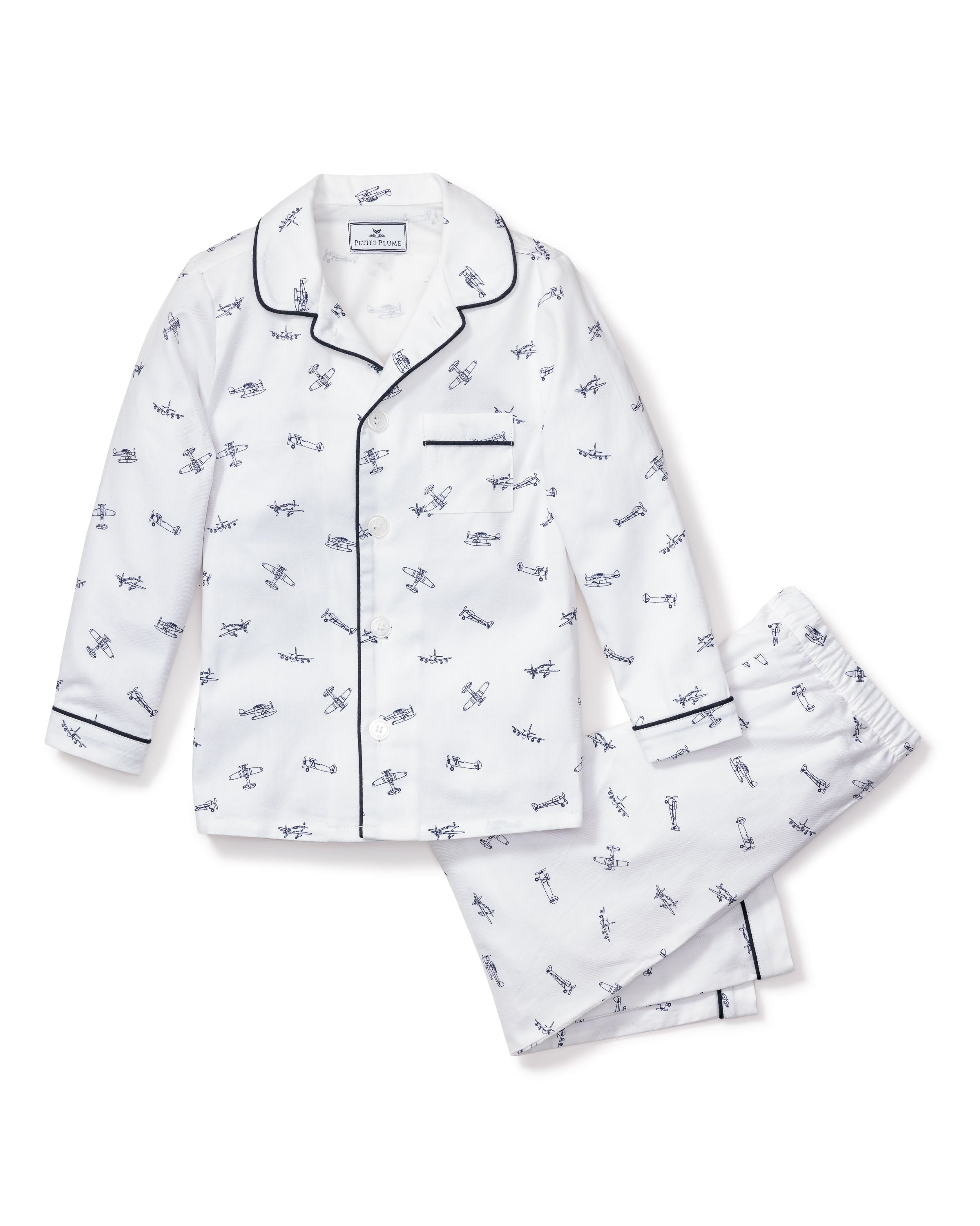 Petite Plumes Kids Twill Pajama Set in Par Avion showcases a classic navy and white airplane design, featuring a long-sleeve button-up top with a chest pocket and matching full-length pants, both accented with navy trimming on the cuffs and collar.