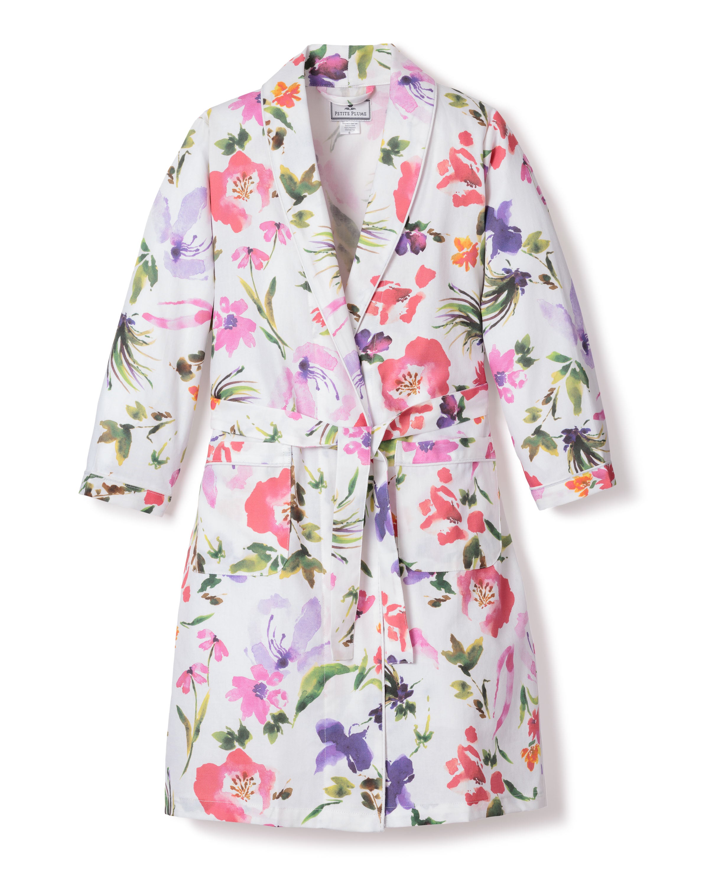 The Kids Twill Robe in Gardens of Giverny by Petite Plume features a floral pattern on a white background with pink, purple, red, and green flowers and leaves. Made from flame-retardant cotton for safety, it includes long sleeves, a collar, and a belt.