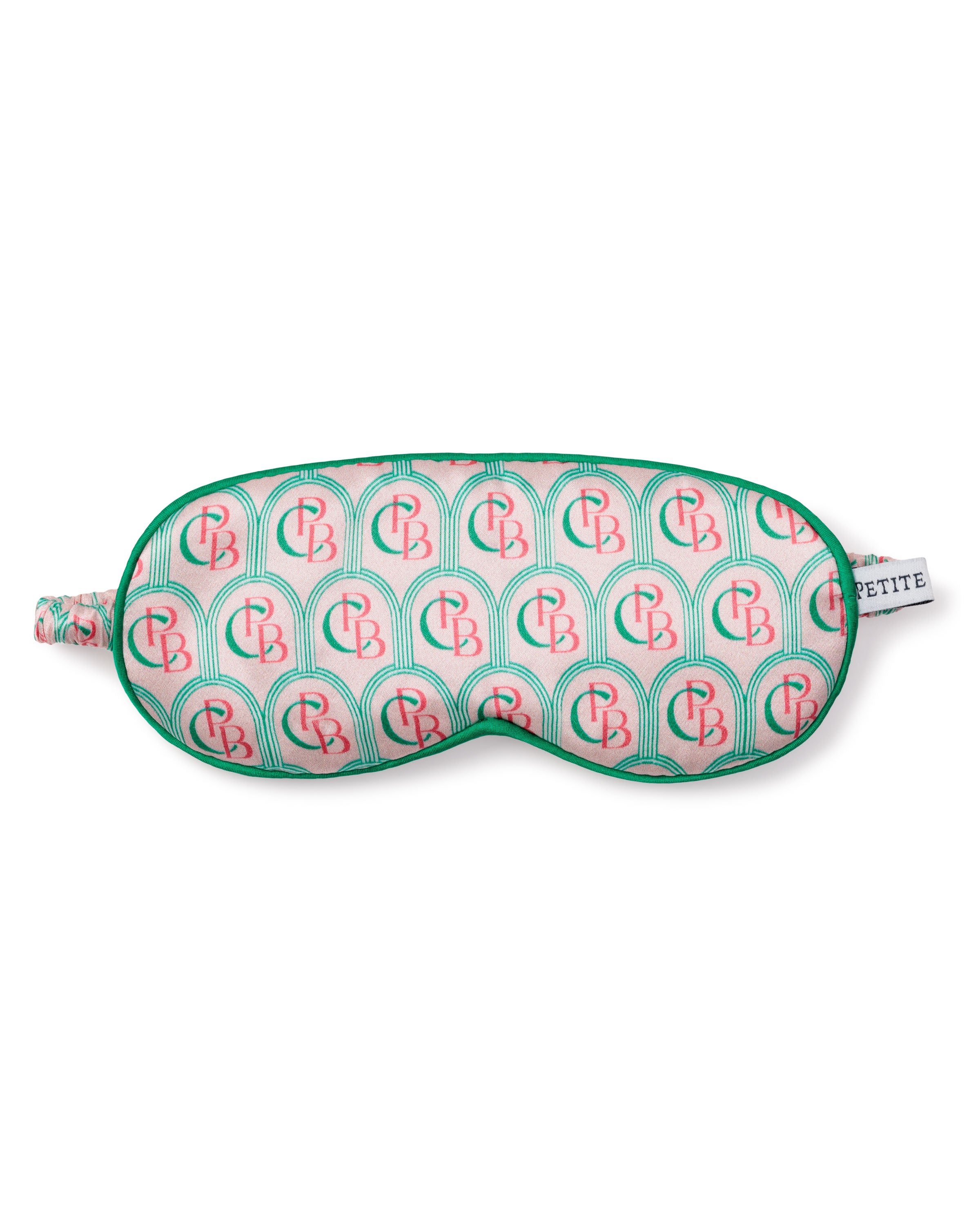 A pure silk sleep mask from Petite Plume features a vibrant arch pattern in pink and green with CB initials, a matching green border, and complements the charm of their pajamas. It includes a small tag reading PETITE.